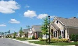 Residential neighborhood with suburban houses, green lawns, and a blue sky with some clouds.