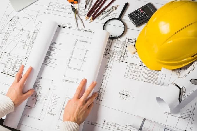 Architectural blueprints and drawings on a construction desk with a yellow safety helmet and tools.