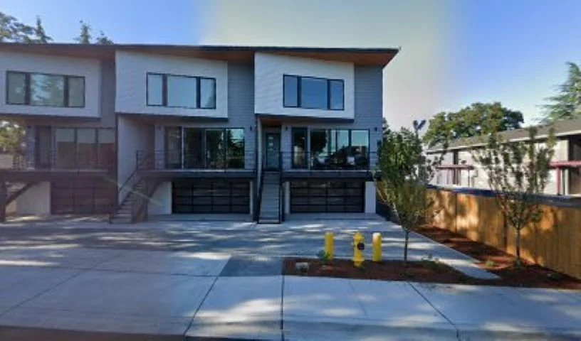 Modern townhouse with large glass windows, a front staircase, and a double garage, surrounded by a paved driveway and landscaped plants.