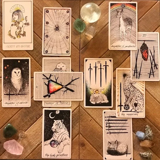 A tarot card reading layout on a wooden surface with various cards, crystals, and stones, including the Sun, Moon, and star-themed cards, and cards with animals like a tiger, owl, and deer.