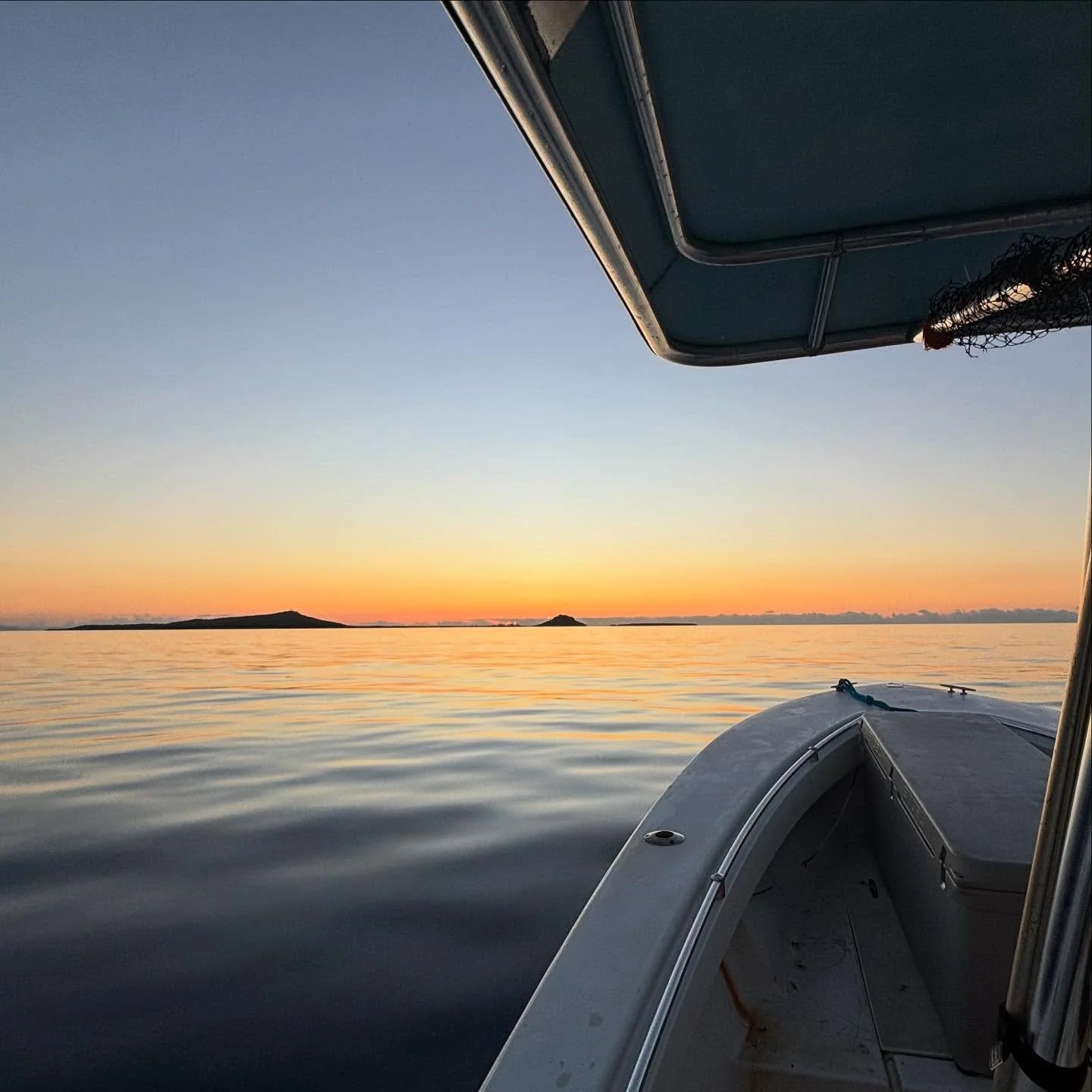 A boat on calm water during sunset, with distant islands and a clear sky.