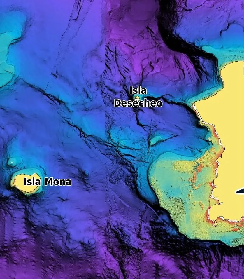 Colorful topographic map of a coastal region with labeled islands: Isla Mona, Isla Desecheo, and Isla. The map displays elevation or bathymetric data with various colors indicating different altitudes or depths.