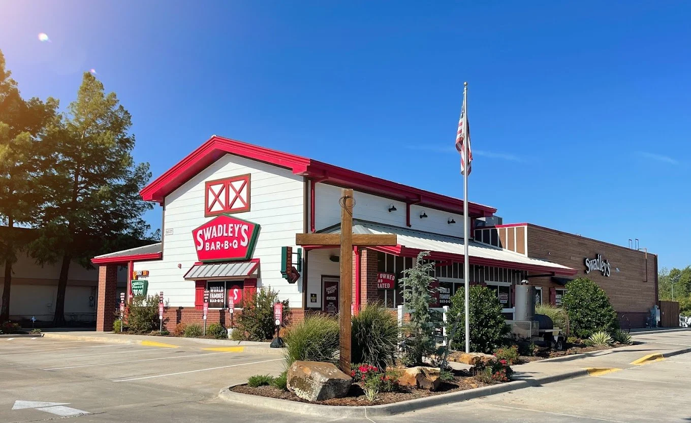 Exterior of Swadley's Barbecue restaurant with parking lot, trees, and flagpole under a clear blue sky.