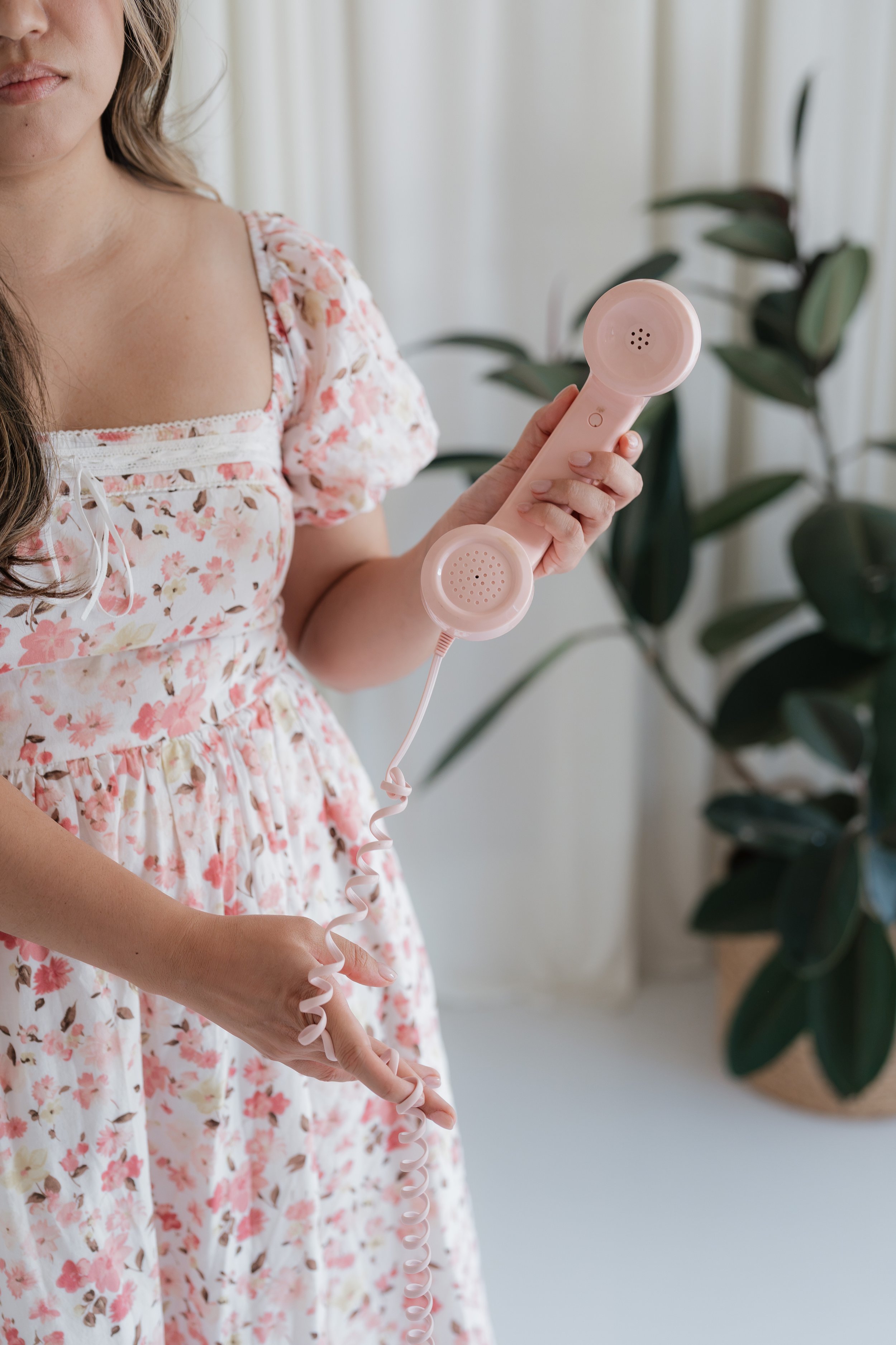 Therapist in a floral dress holding a pink phone to book a free consultation
