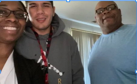 Three people smiling at the camera, a woman on the left, a young man in the middle, and an older man on the right, indoors with curtains in the background.