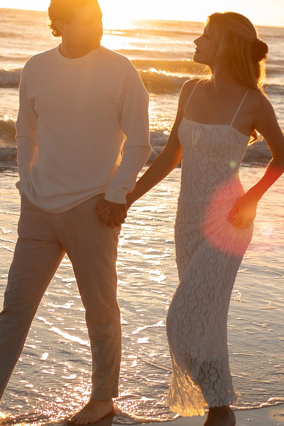 A couple holding hands on the beach at sunset, with the ocean in the background.
