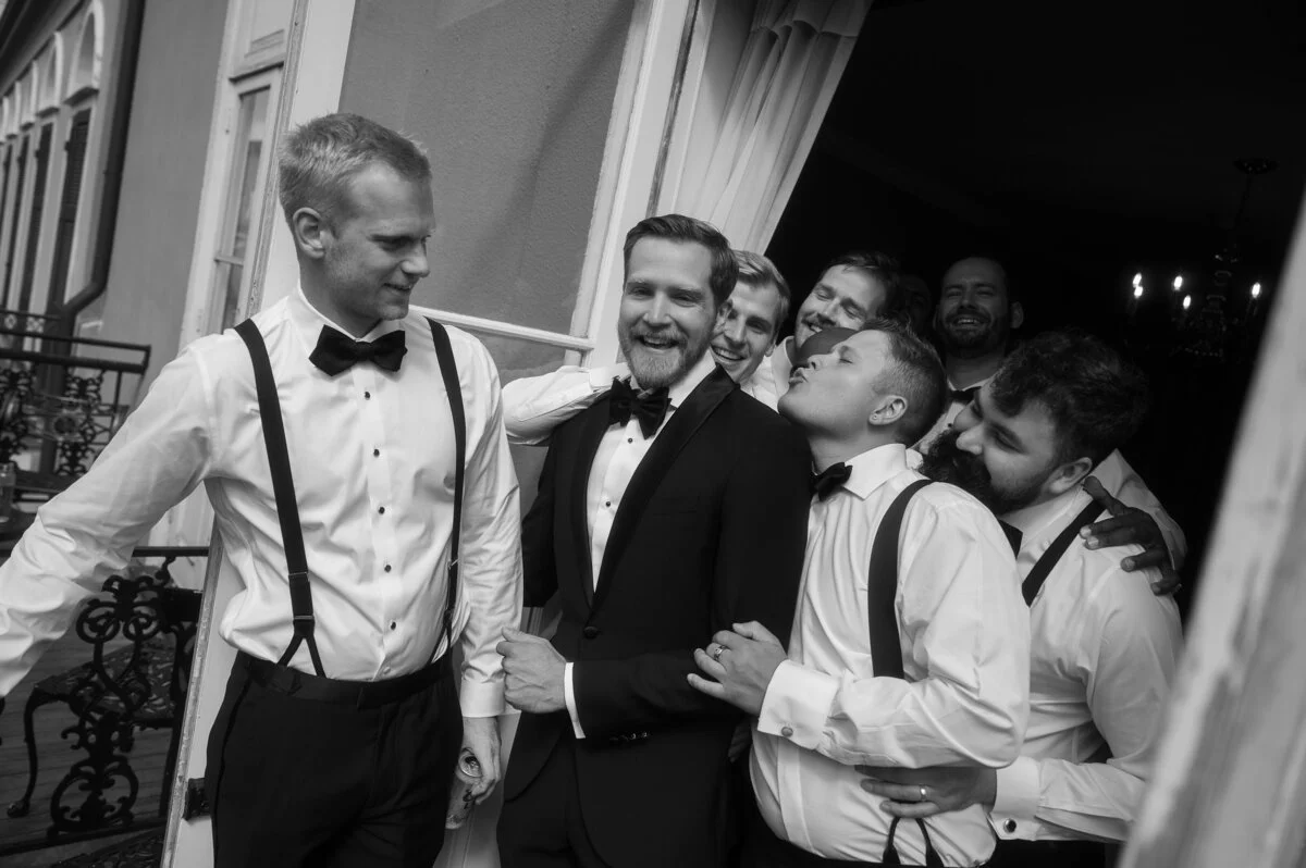 A group of men dressed in tuxedos and bow ties laughing and smiling together during a celebration or wedding party.