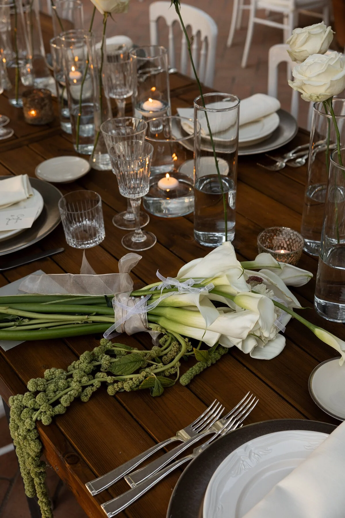 A beautifully set dining table with white flowers, glassware, candles, plates, and cutlery for a formal event.