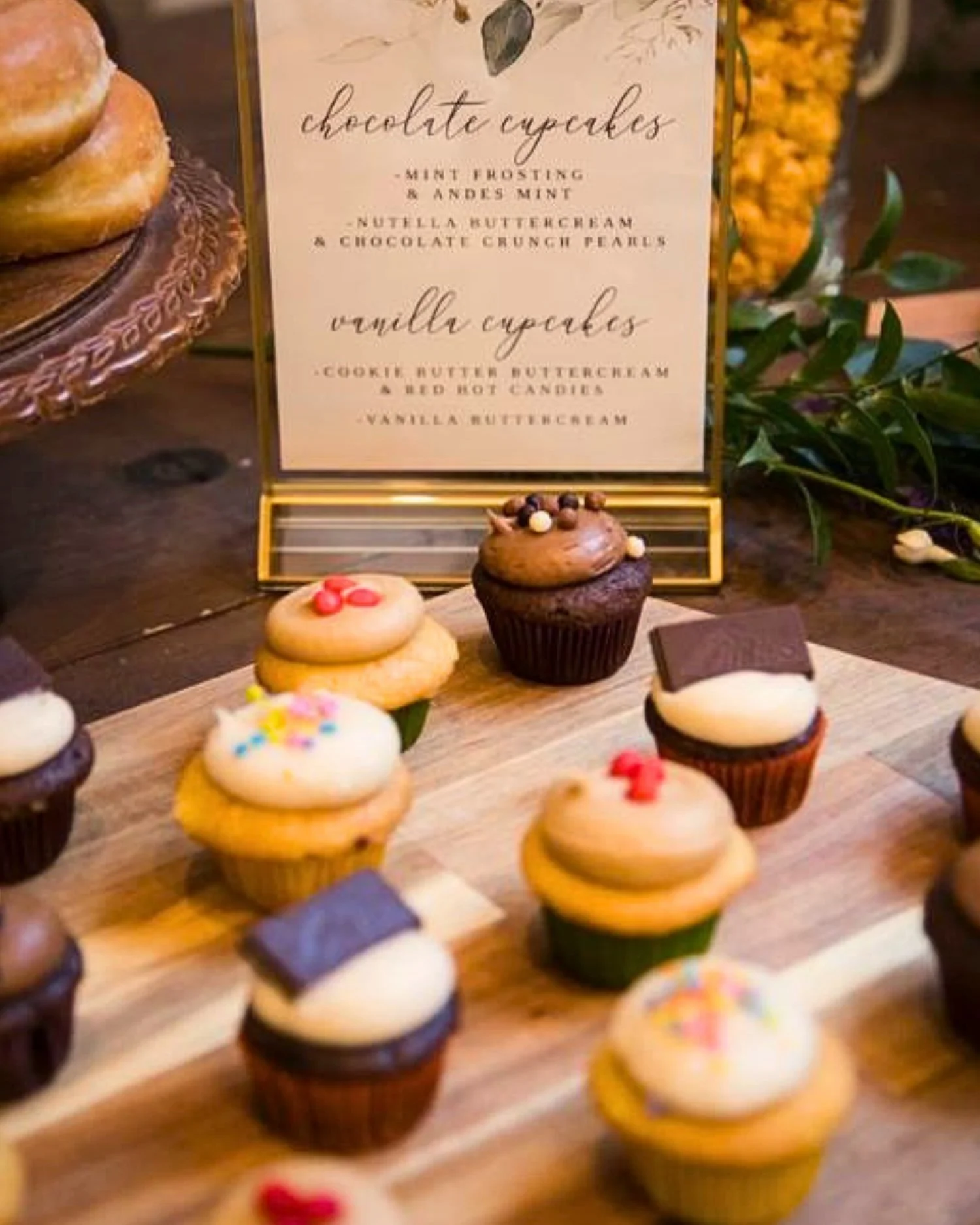 Assorted mini cupcakes with various frosting colors and decorations on a wooden tray.