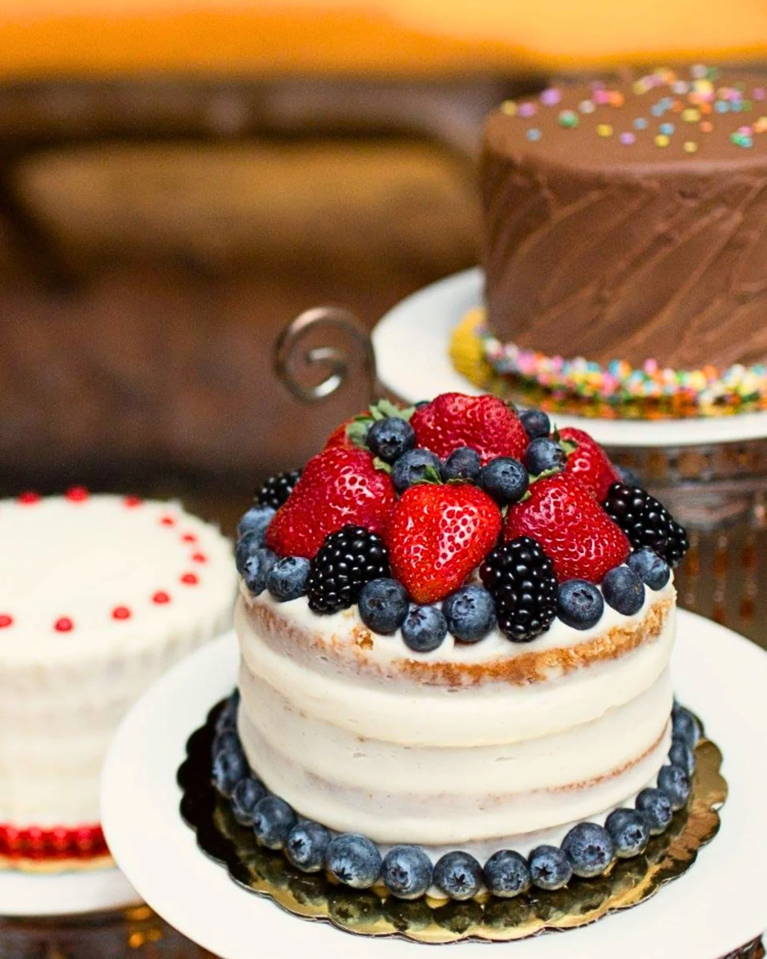 Cake topped with Barries, Chocolate cake with sprinkles, and a white buttercream frosted cake
