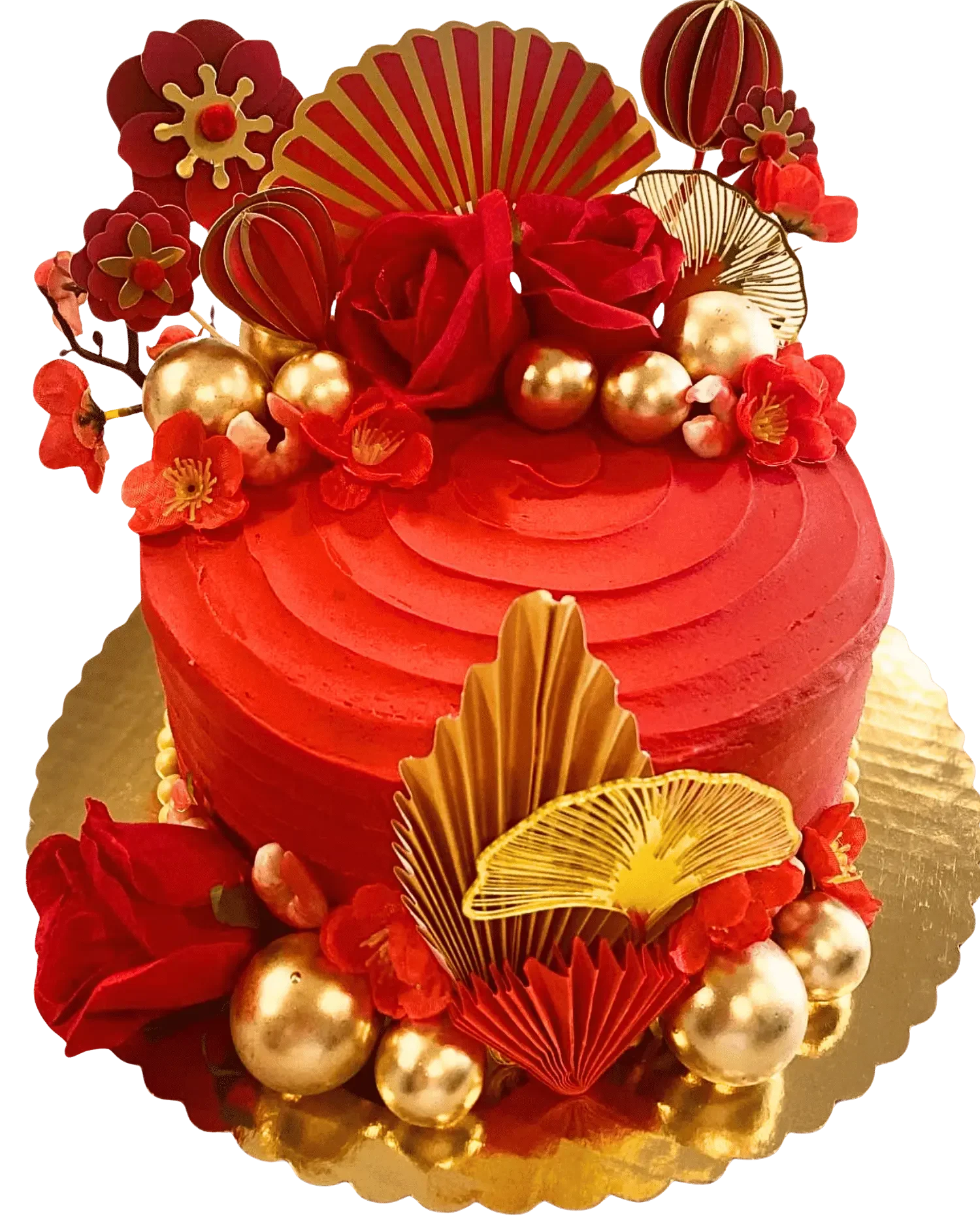 A decorative cake with an Asian Hibac red and gold color theme. The cake is topped with red roses, gold and red spherical decorations, and ornate paper fans. The base of the cake is surrounded by red flower petals and additional gold and red accents.