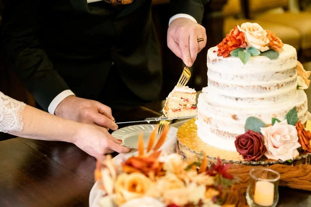 Person in formal attire slices a wedding cake with white icing and floral decorations.