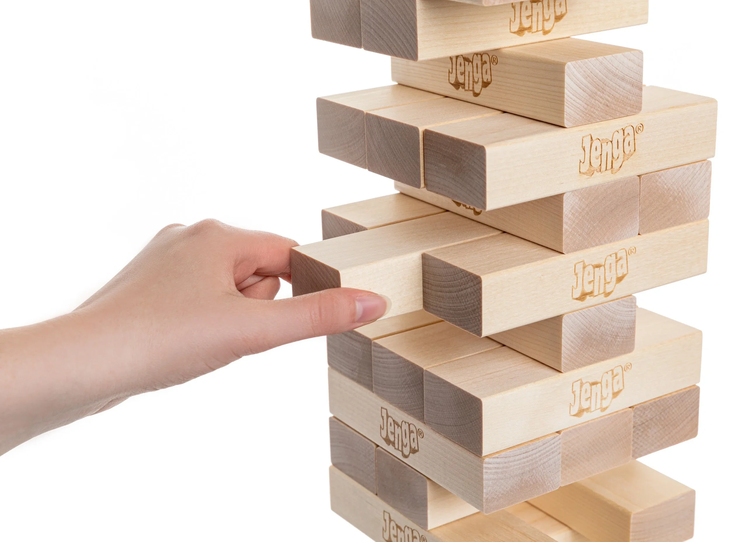 A person is holding a wooden Jenga block near a partially completed Jenga tower, with several wooden blocks stacked vertically and some blocks branded with the Jenga logo.