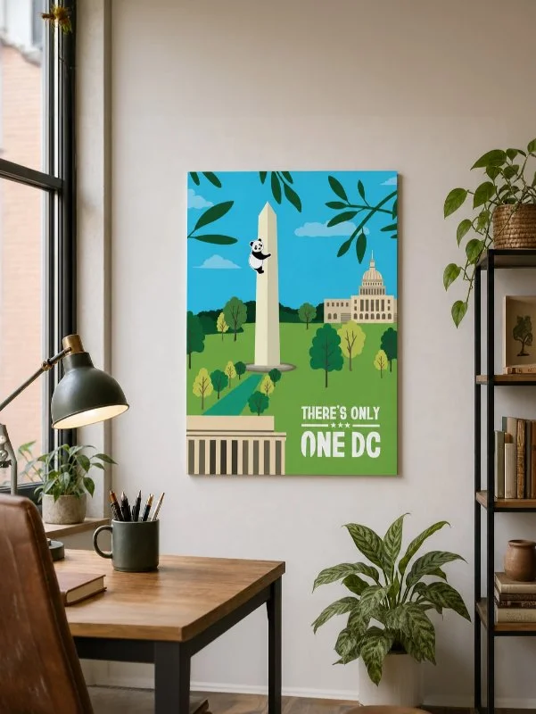 Destination DC 'There's Only One DC' Washington Monument and panda climbing illustration printed poster hanging on an office wall mockup above a wooden desk with plants and a bookshelf.