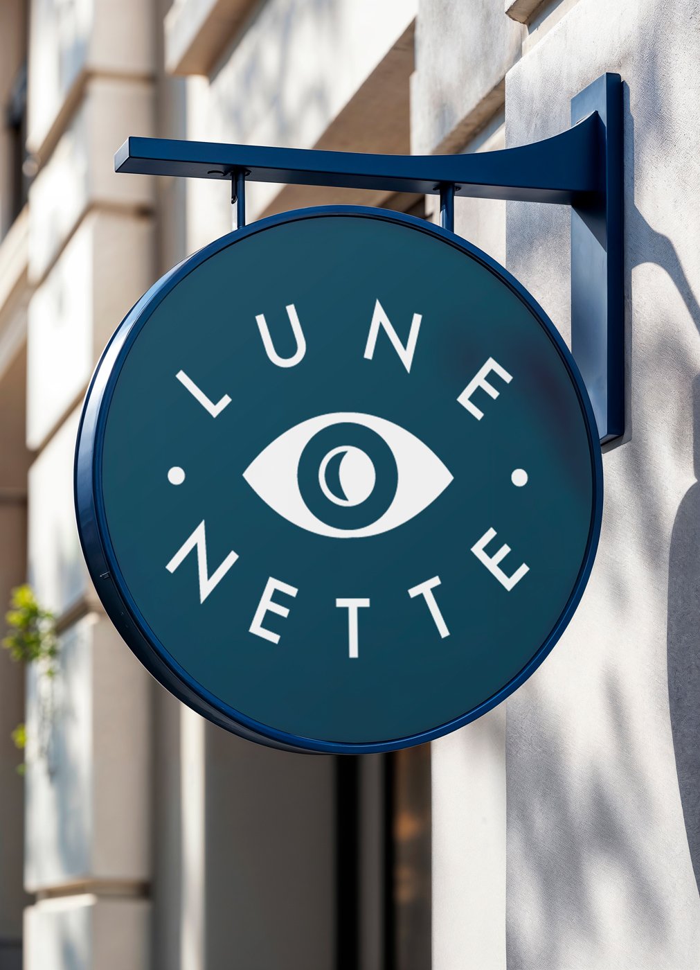 Lune Nette optometry brand logo design displayed on a round deep teal navy projecting storefront sign featuring a stylized eye icon with crescent moon pupil mounted on a building exterior.