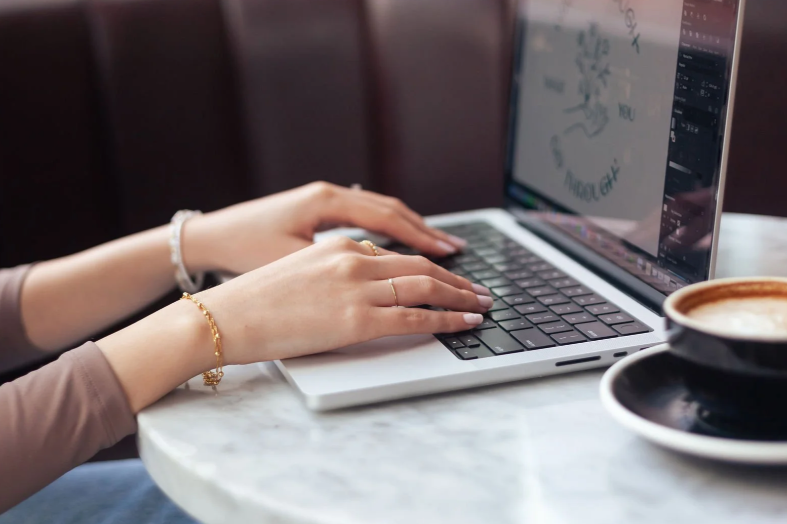 Yasmine Design Co. – Graphic Designer working from a café behind the scenes using laptop and Illustrator app to create digital illustrations.