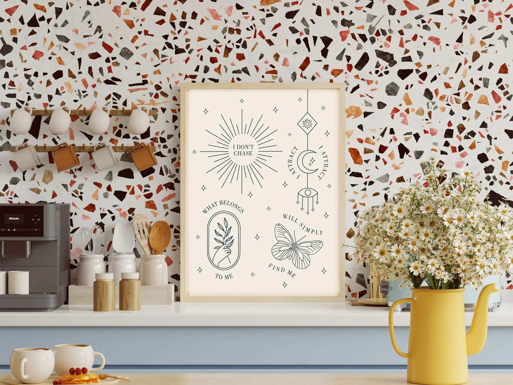 Law of attraction and manifestation motivational art print in a wood frame displayed on a kitchen counter, featuring celestial fine-line illustrations of a sun, moon, butterfly, and botanical hand with the affirmation.
