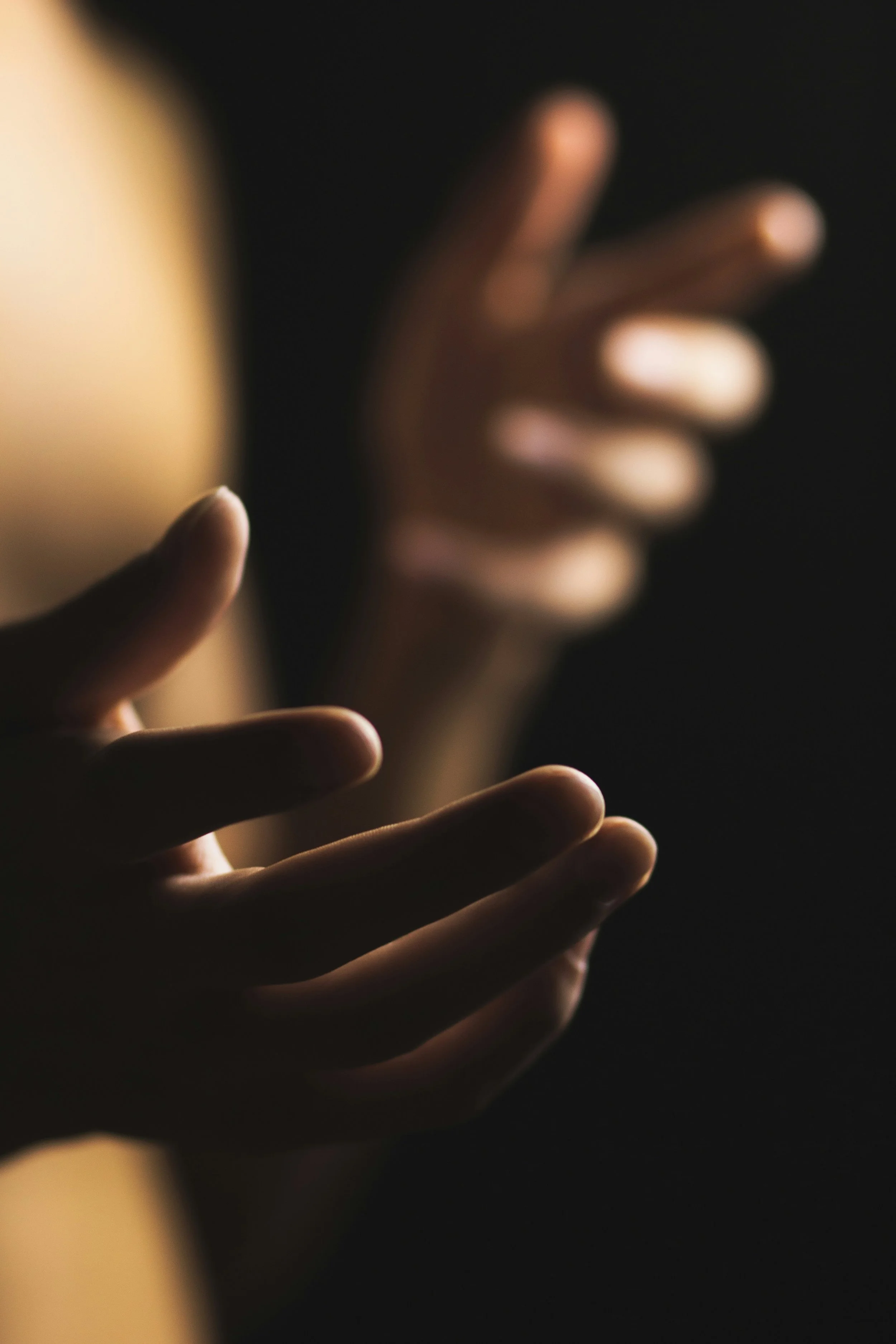 Close-up of two hands reaching towards each other against a dark background, with one hand slightly more in focus than the other.