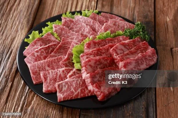Plate of raw marbled Wagyu beef slices with lettuce and parsley on a wooden table.