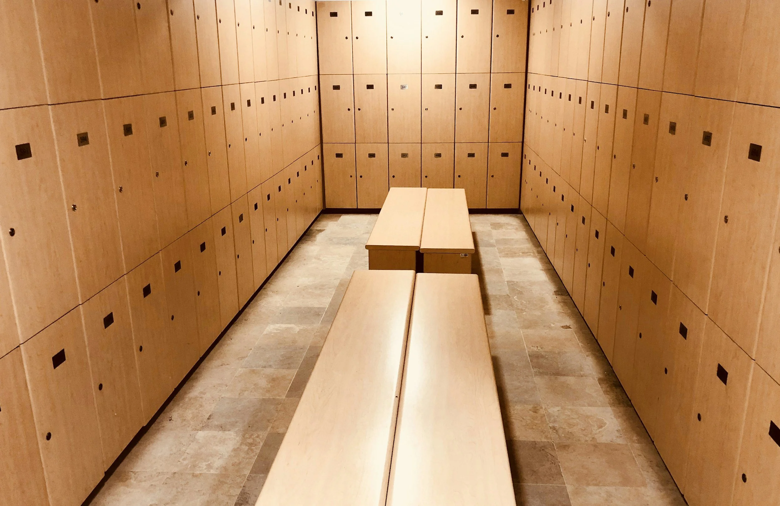 Wooden lockers with black combination locks in a locker room, with two wooden benches in the center.