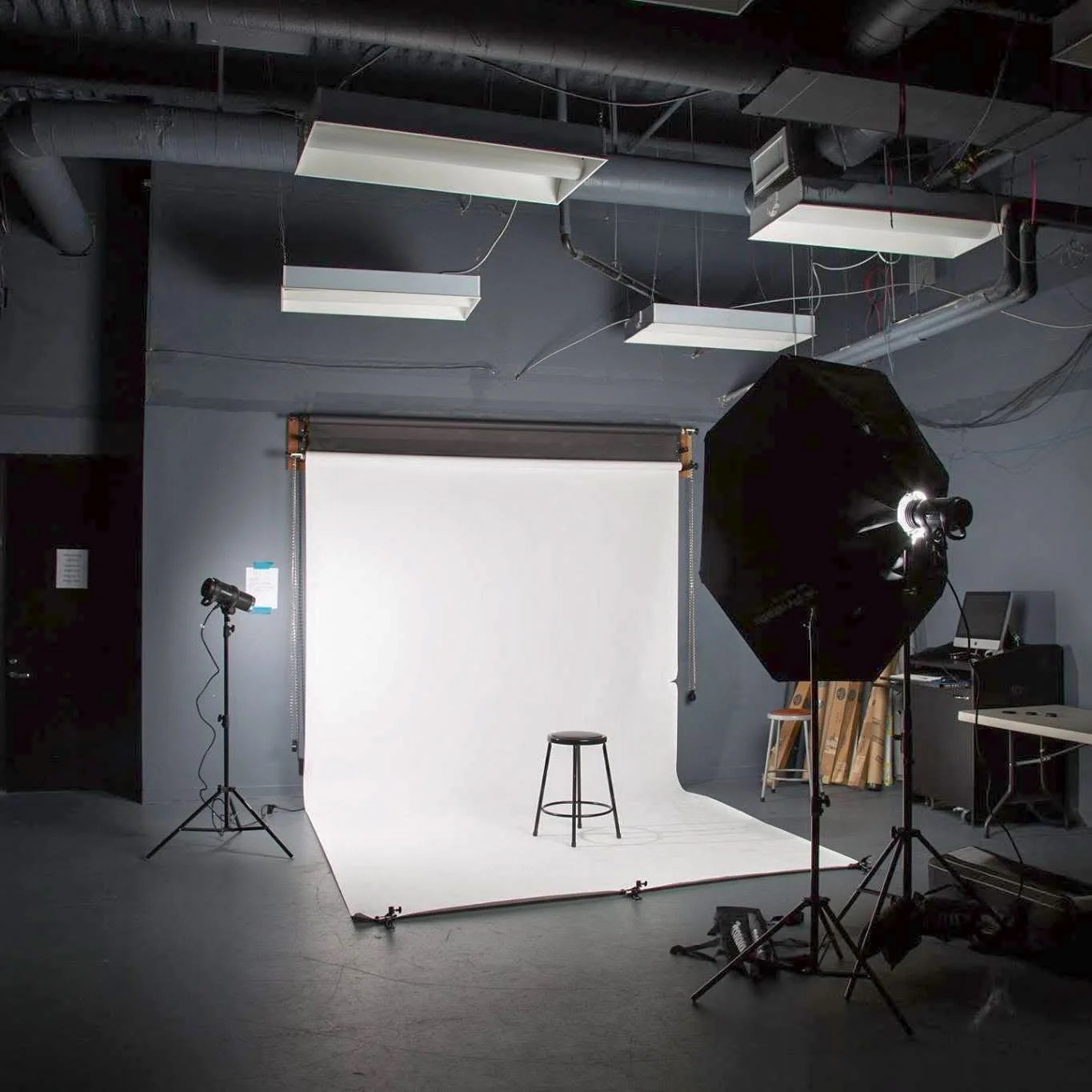 Photo of a photography studio with a white backdrop, studio lights, and a stool, set up for a photo shoot.