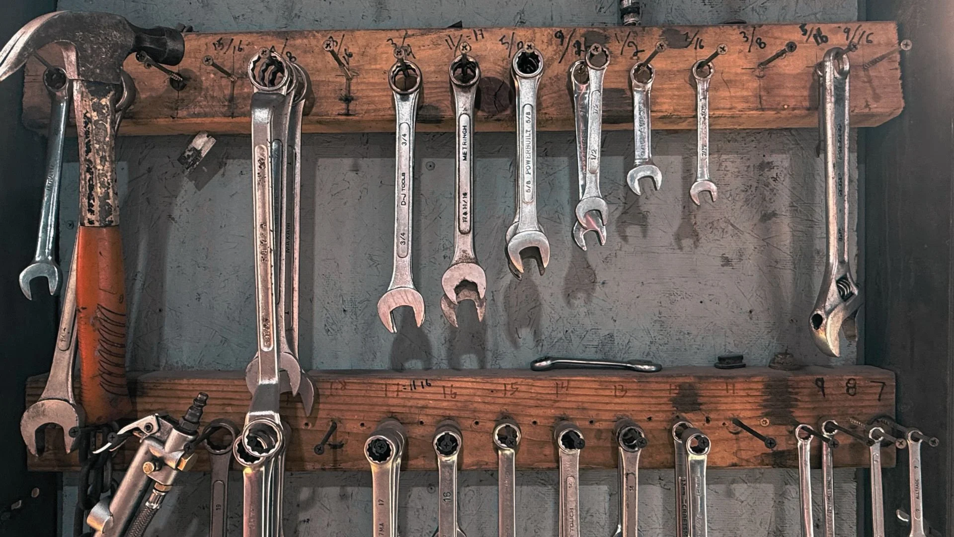Organization of hand tools, including wrenches and a hammer, hanging on a wooden wall with labelled hooks.