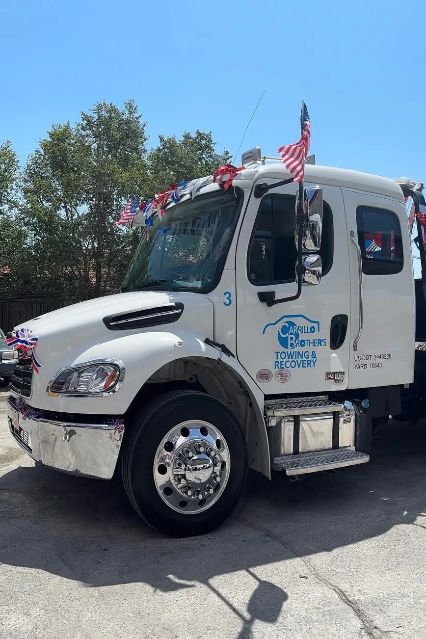A white tow truck decorated with American flags and red, white, and blue ribbons.