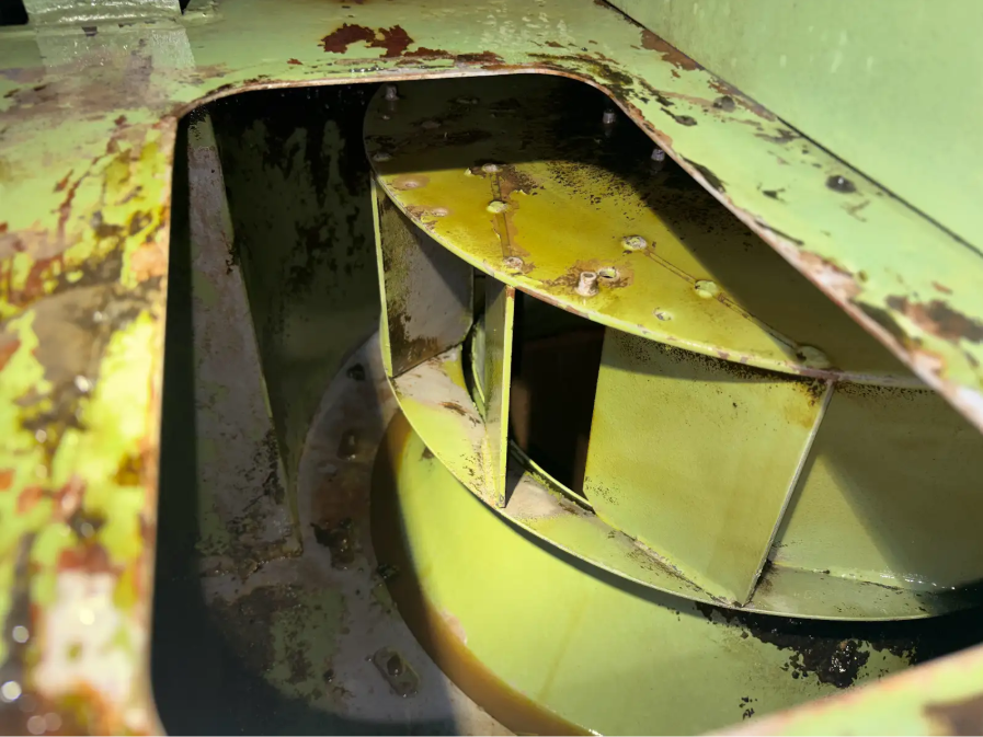 Close-up of a metal mechanical component with green and yellow paint, showing rust, grime, and worn surfaces.