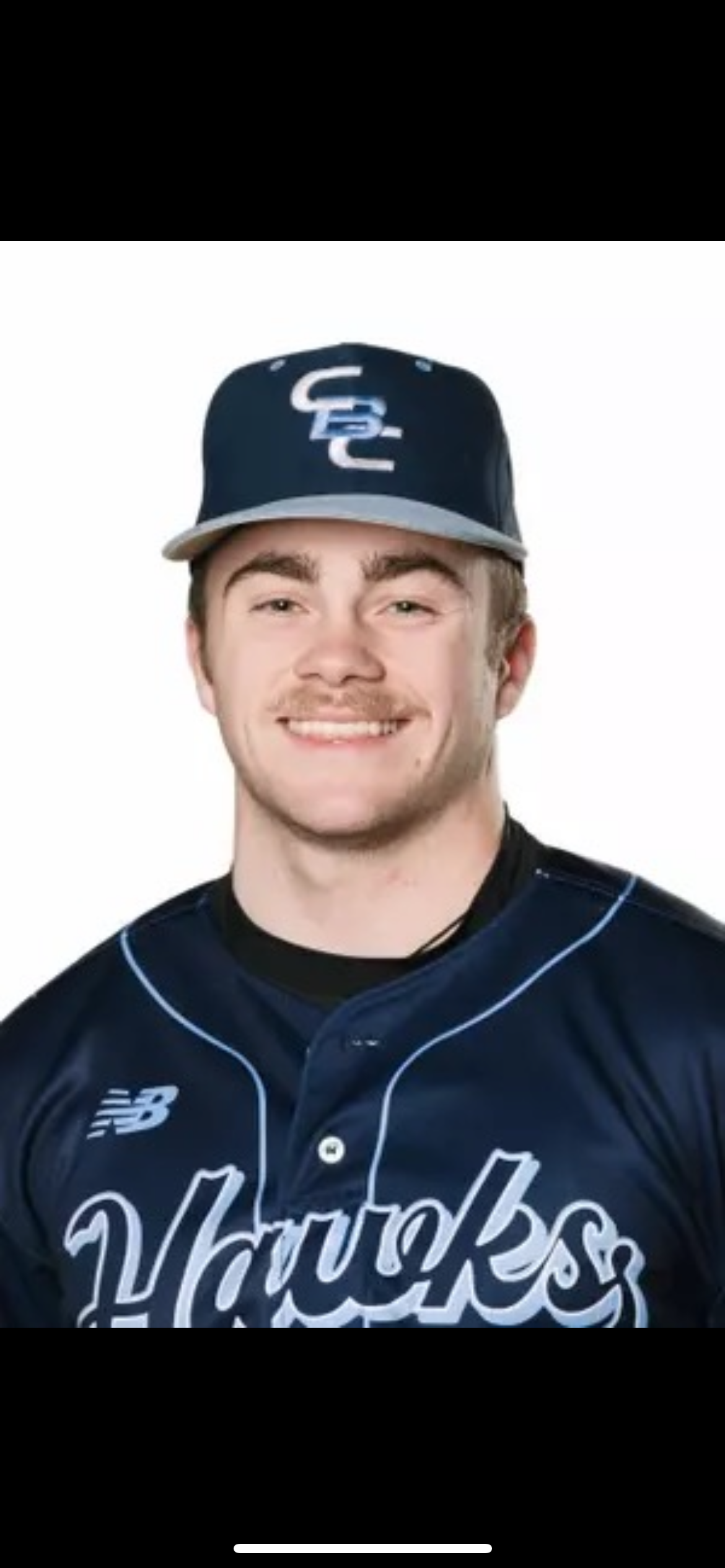 A young man smiling, wearing a navy blue baseball cap with a logo and a navy blue sports jersey with white lettering and logos.