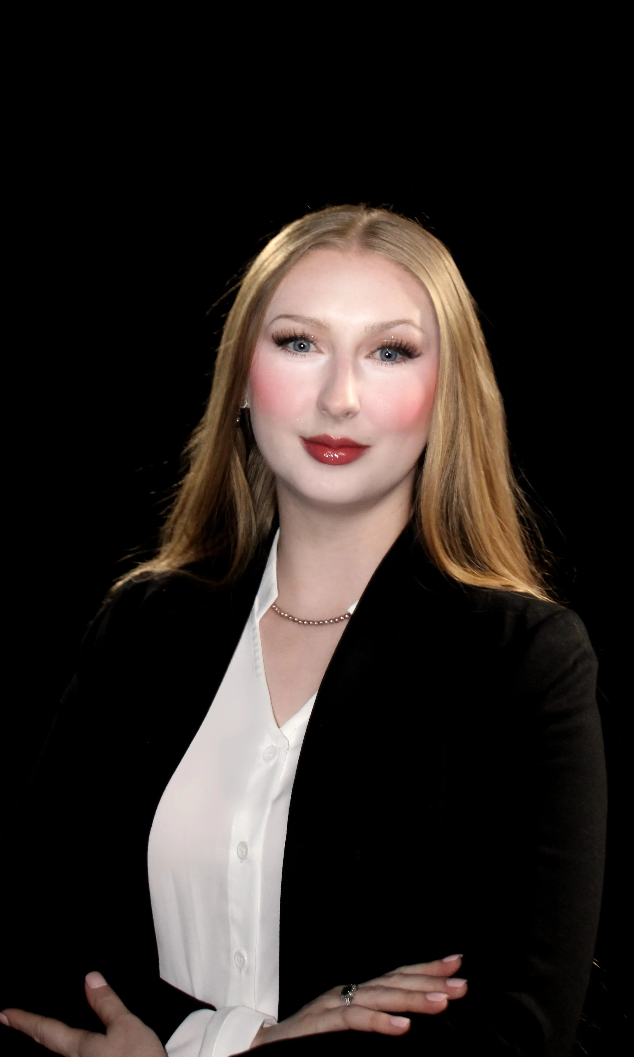 The CEO, a pale female with long, wavy red/blonde hair, wearing a black blazer over a white blouse, standing against a black background. Patient Care Advocacy. Florida. Healthcare Navigation Services. Insurance Navigation Services.