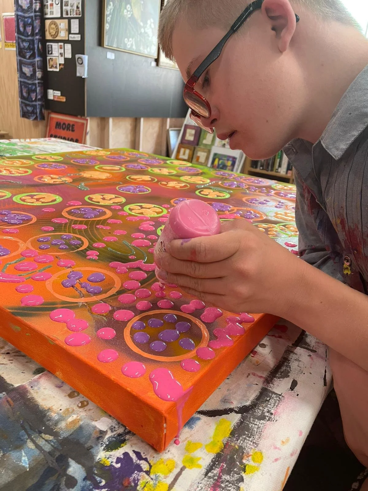 close up of wade Keighley squeezing a bottle of pink paint on to a canvas that is covered in bright circles and dots