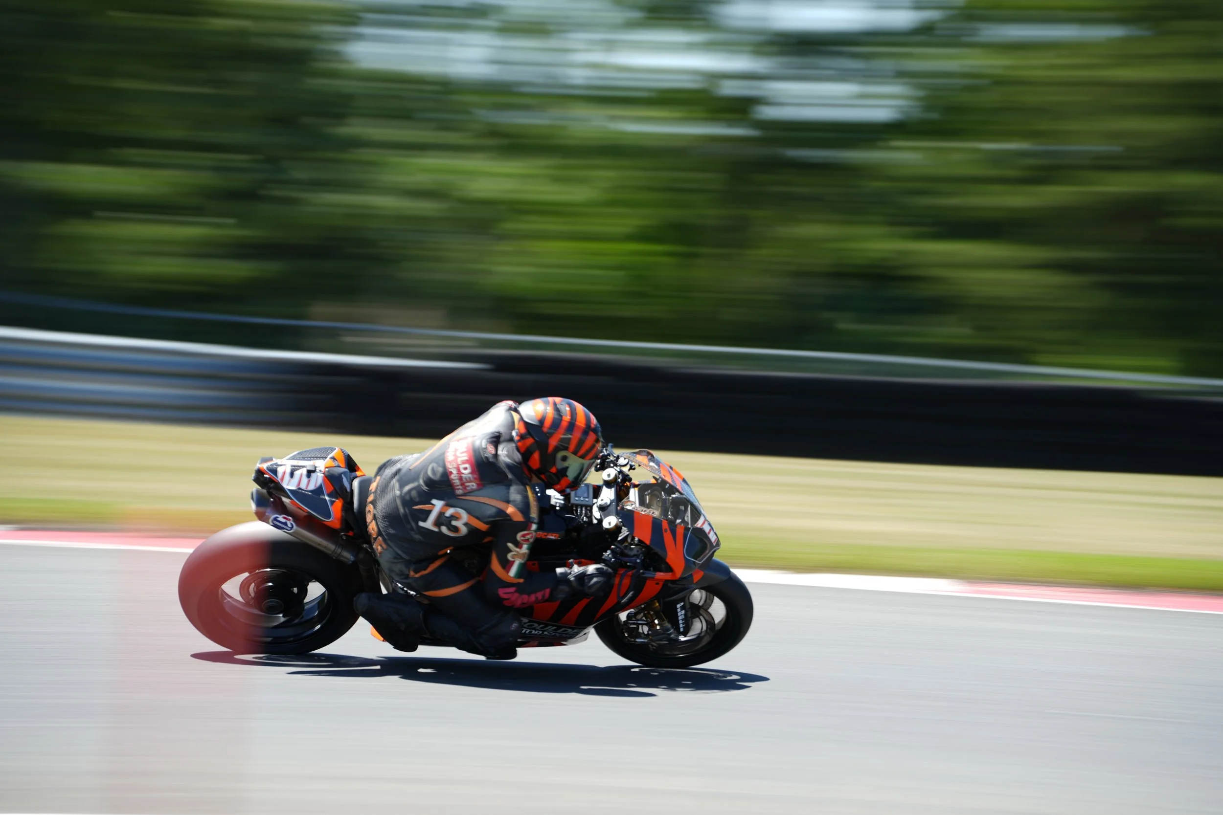 Motorcycle racer in racing gear speeding on a track with blurred green background.