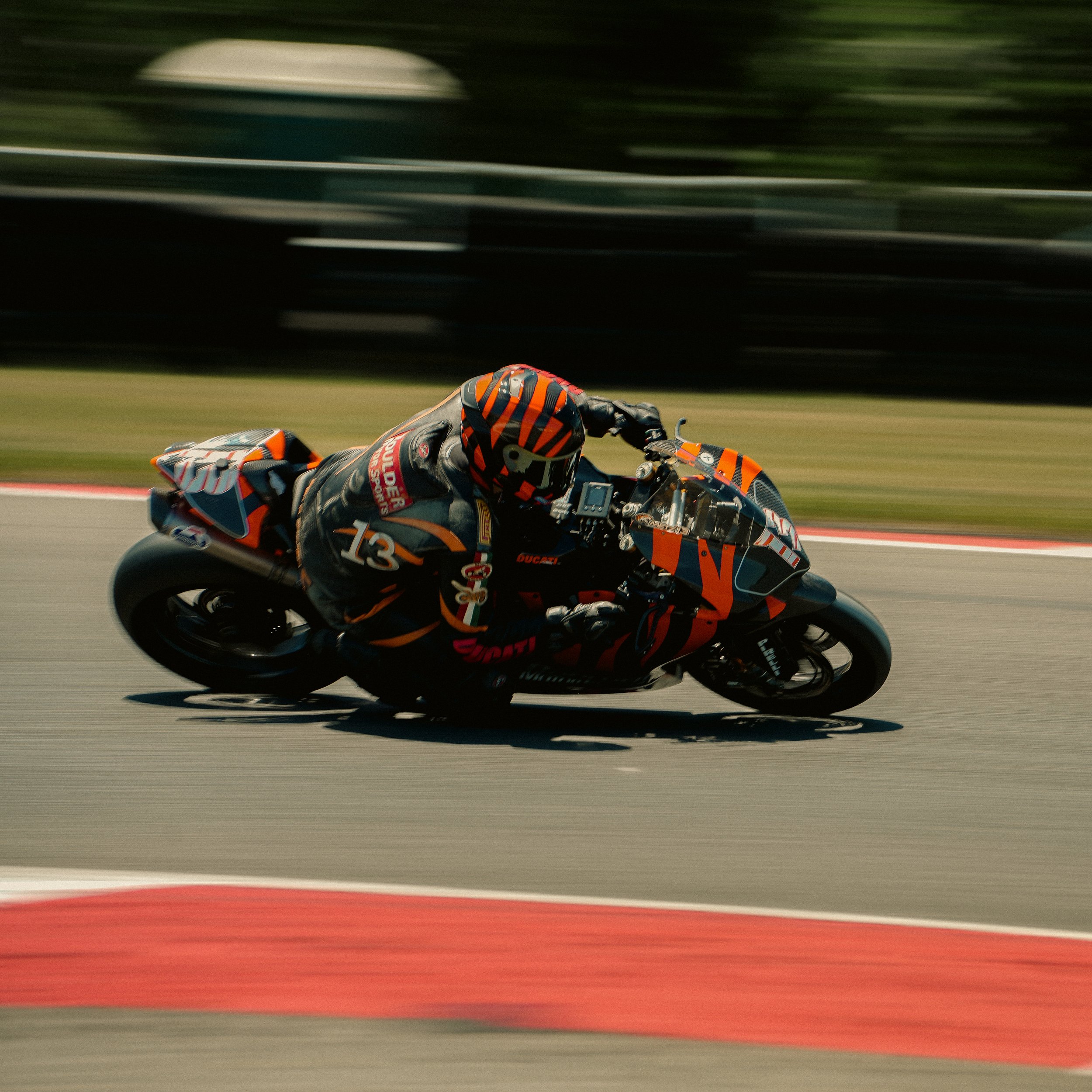 Motorcycle racer in black and orange suit and helmet leaning into a turn on a racetrack with a blurred background.