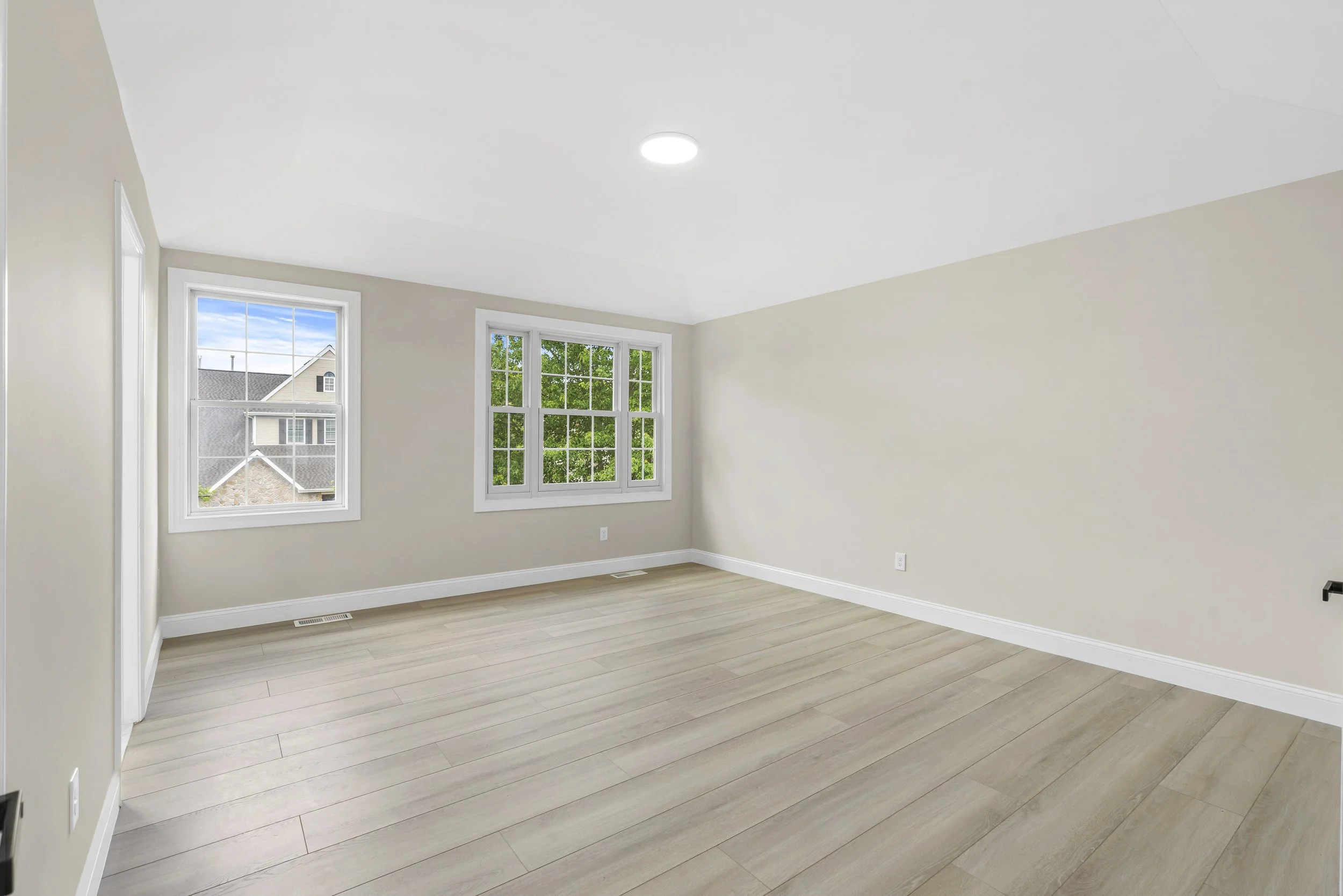 Empty room with two windows, beige walls, and light wooden flooring.