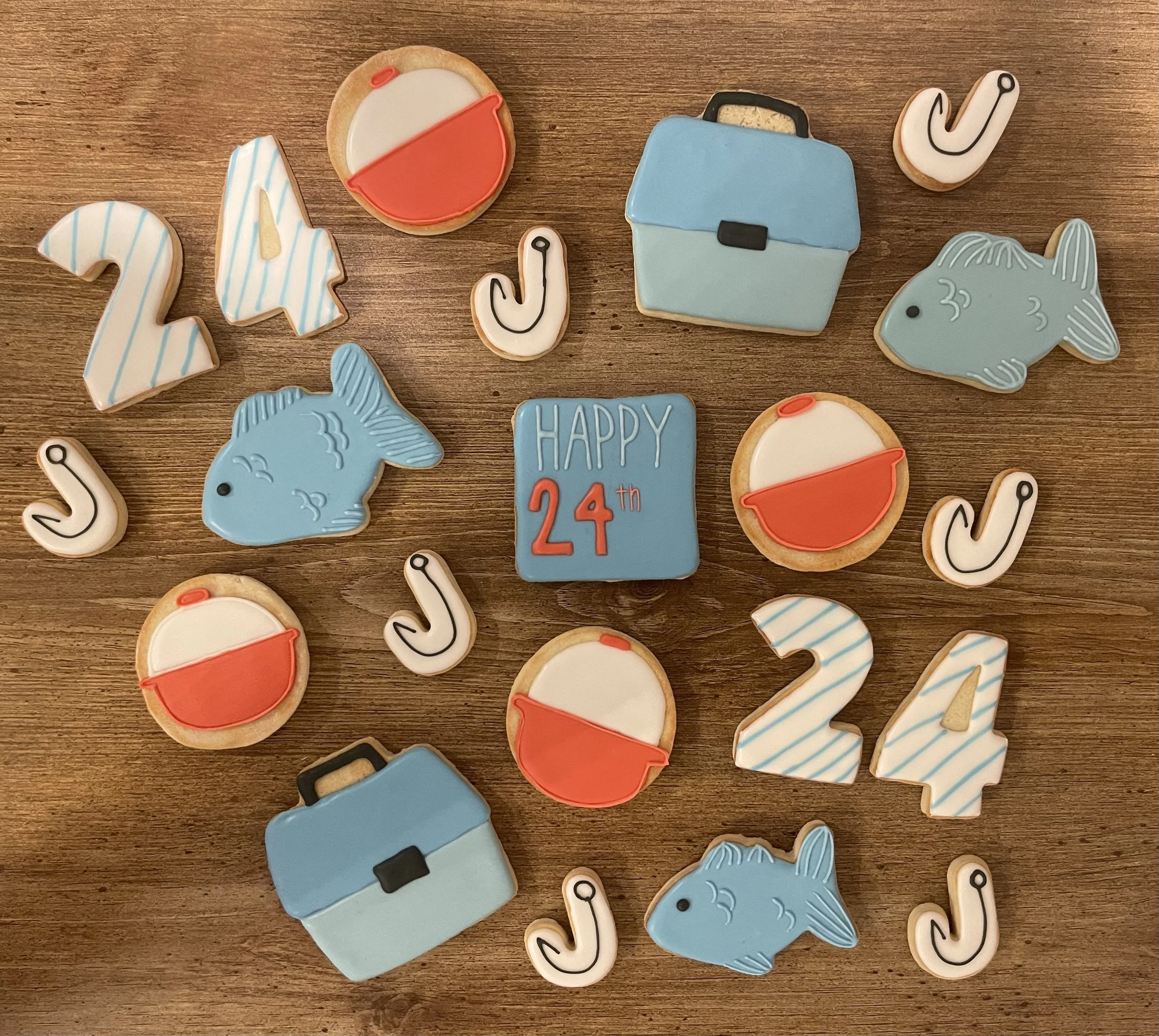 Decorated cookies on a wooden surface with various designs including ice cream, fish, locket, and text that says "HAPPY 24th".