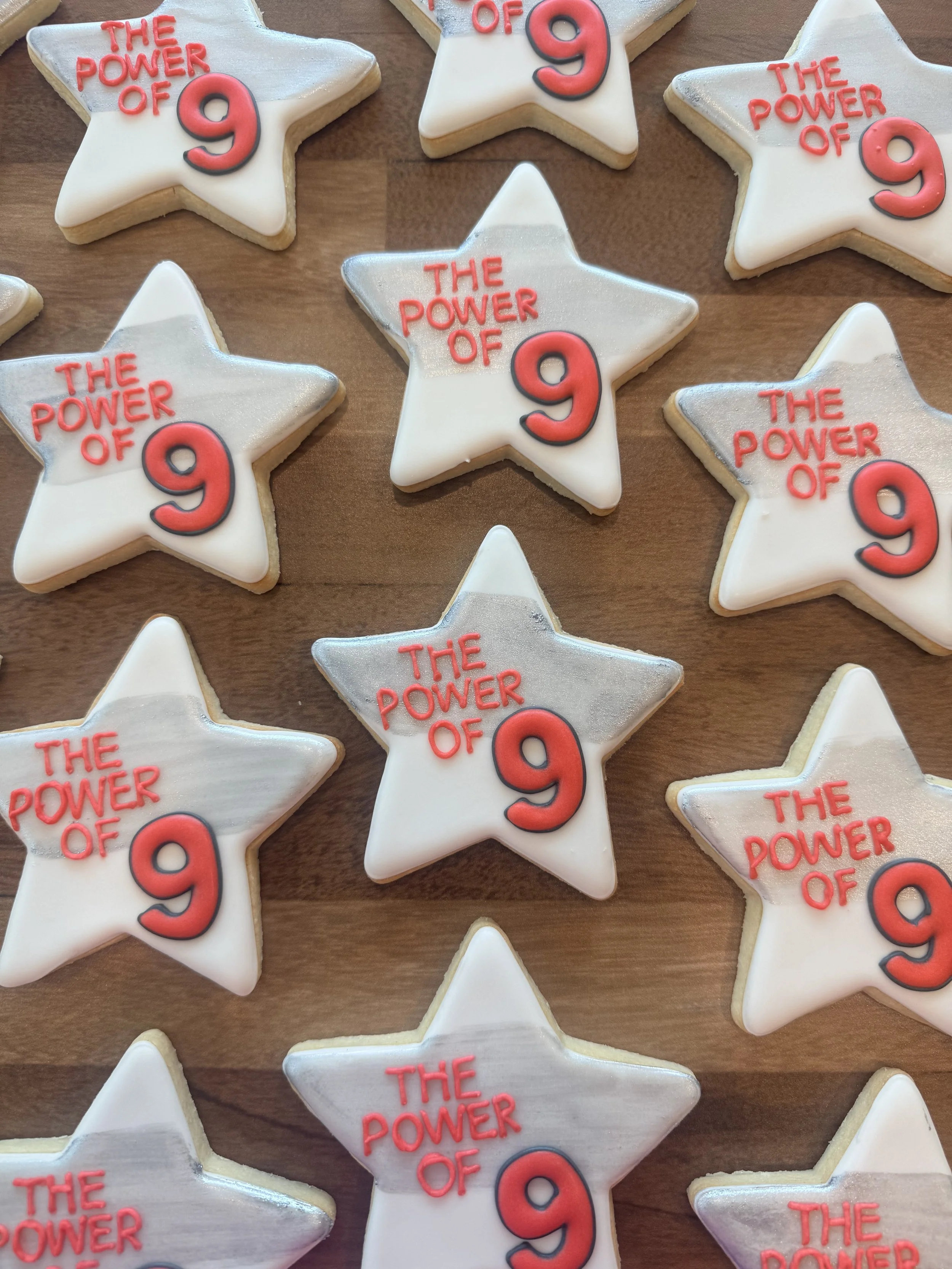 Star-shaped cookies with white icing, decorated with red and black lettering reading "The Power of 9".