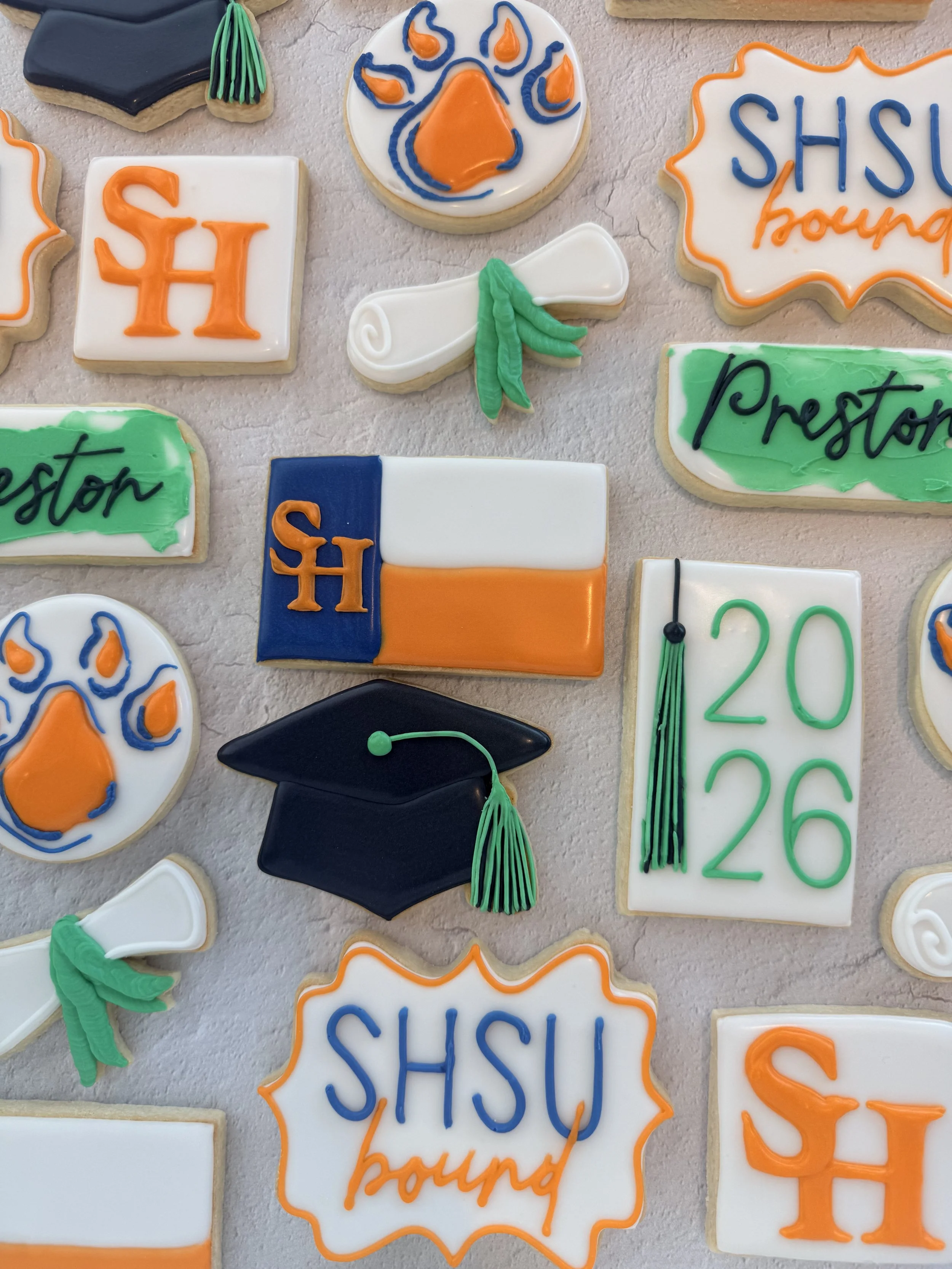 Assorted decorated cookies for Shsu (Sam Houston State University) graduation, featuring caps, diplomas, the university logo, and message cookies.