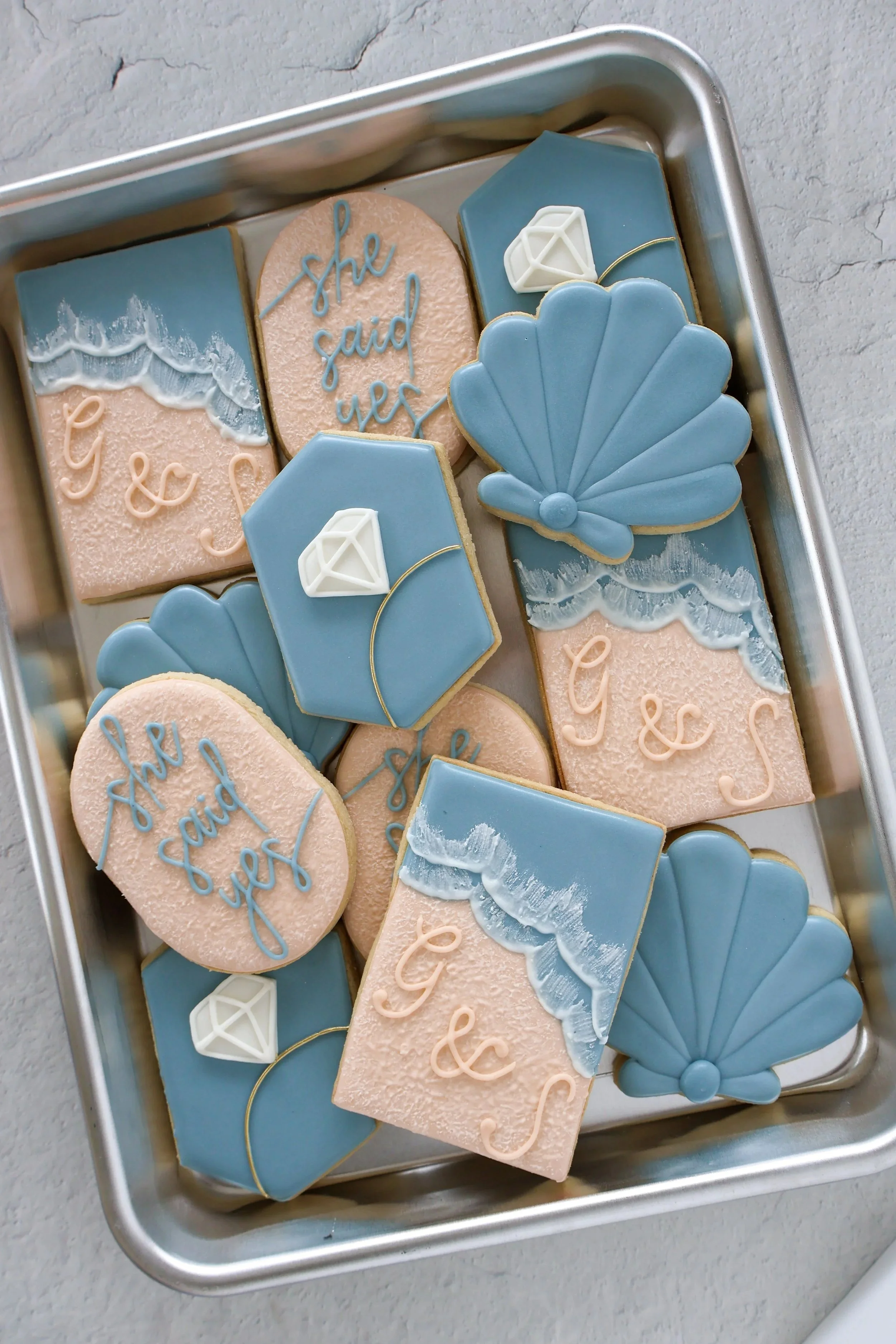 Assorted decorated cookies with ocean and jewelry themes in a metal tray.