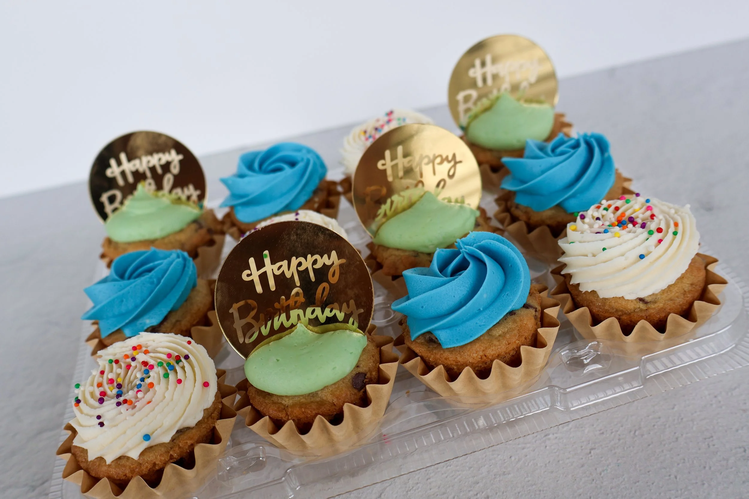 Assorted birthday cupcakes with colorful frosting and sprinkles, some with 'Happy Birthday' toppers.