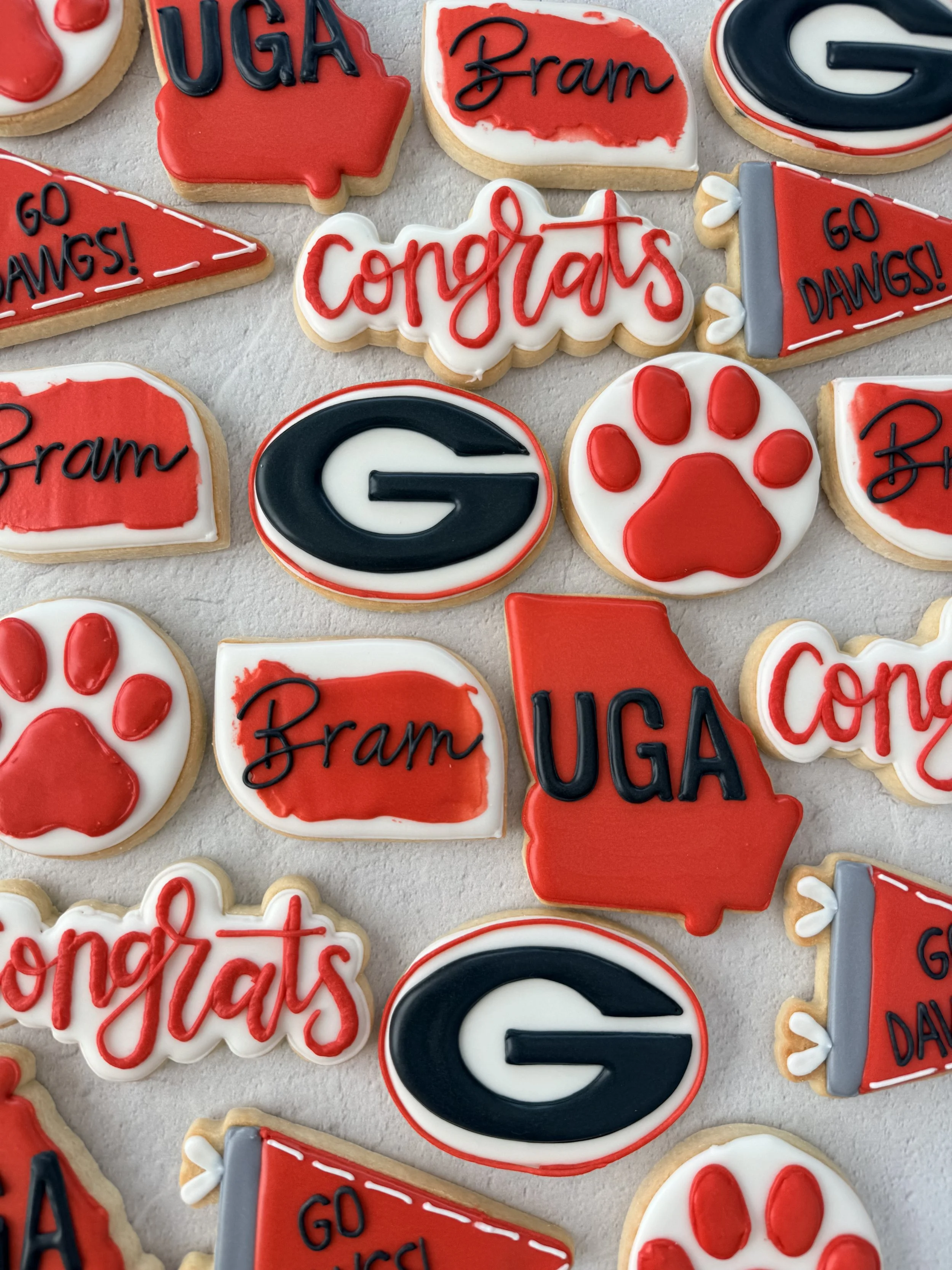 Decorated cookies with UGA, Georgia G logo, paw print, congratulates, and go DAWGS! messages in red, black, white, and gray icing.