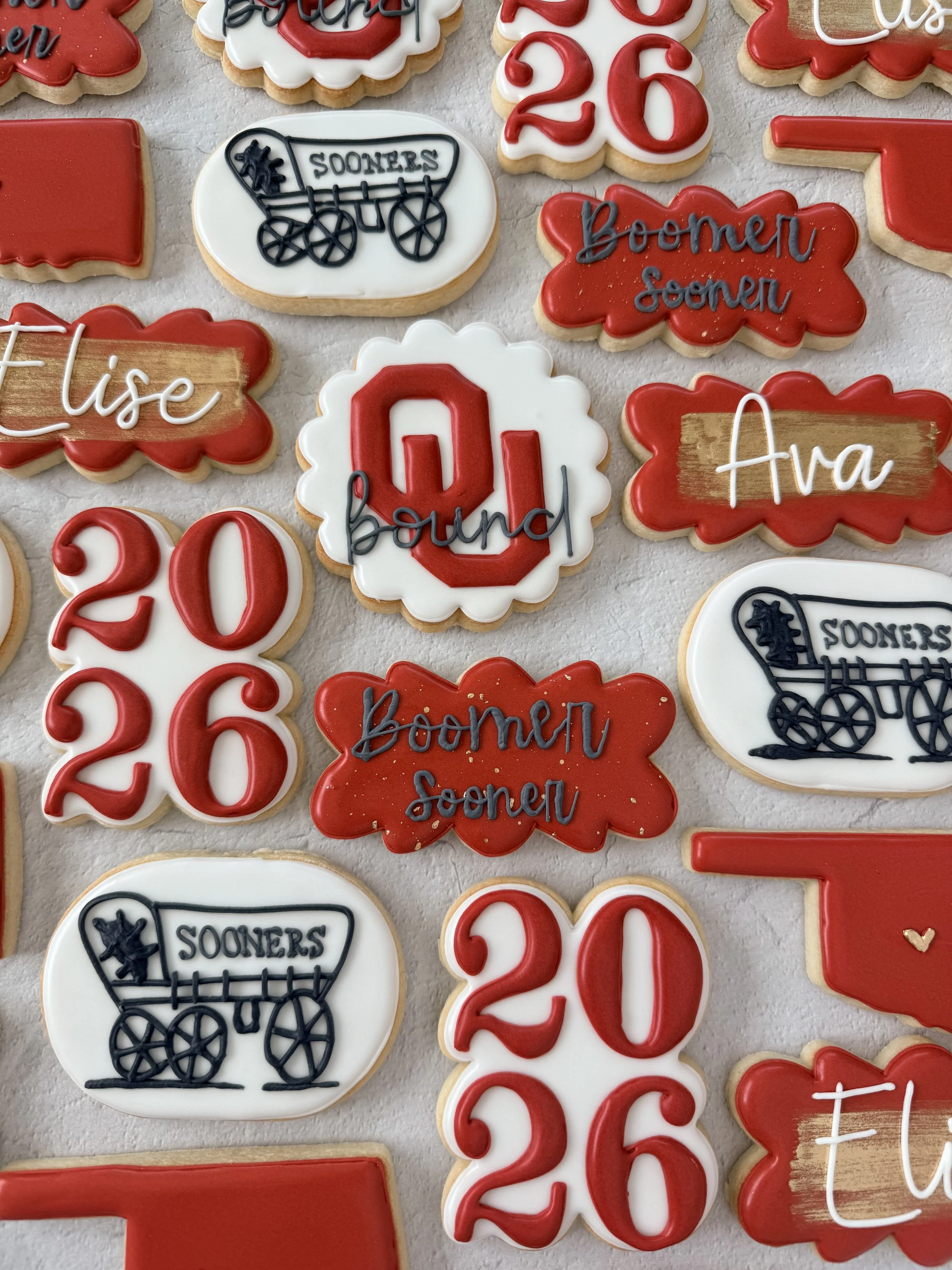 A collection of decorated cookies celebrating a graduation, featuring phrases such as 'Bound' and 'Elise,' the year '2023,' and symbols like a graduation cap and a school wagon with the text 'Sooners'.