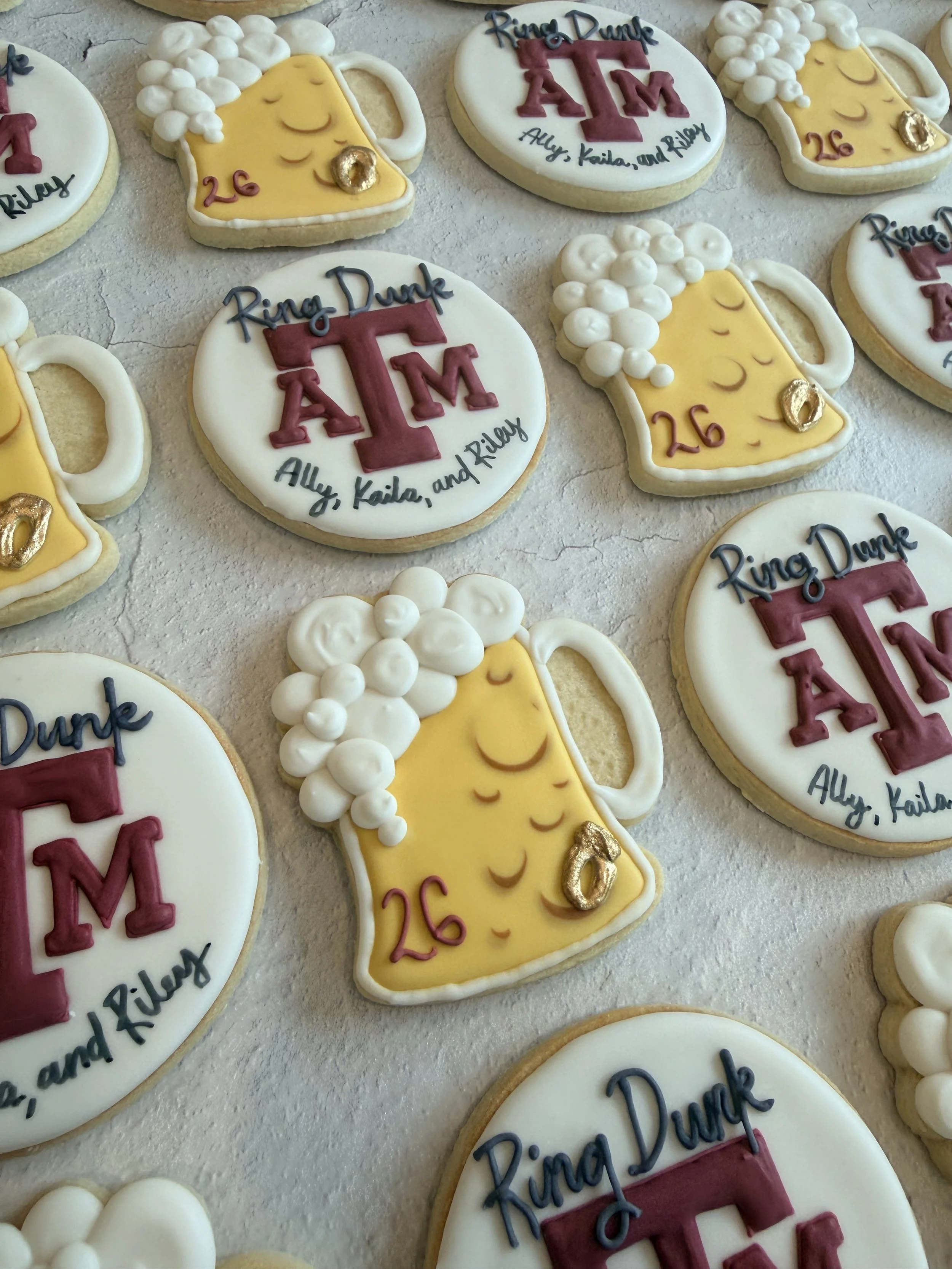 Decorative cookies with the text 'Ring, Duke, ATL, Ally, Kaila, and Riley' and designs of beer mugs and the University of Georgia's Athens campus logo.
