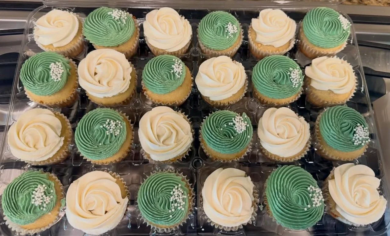 Tray of cupcakes with white and green frosting, decorated with small white sprinkles.
