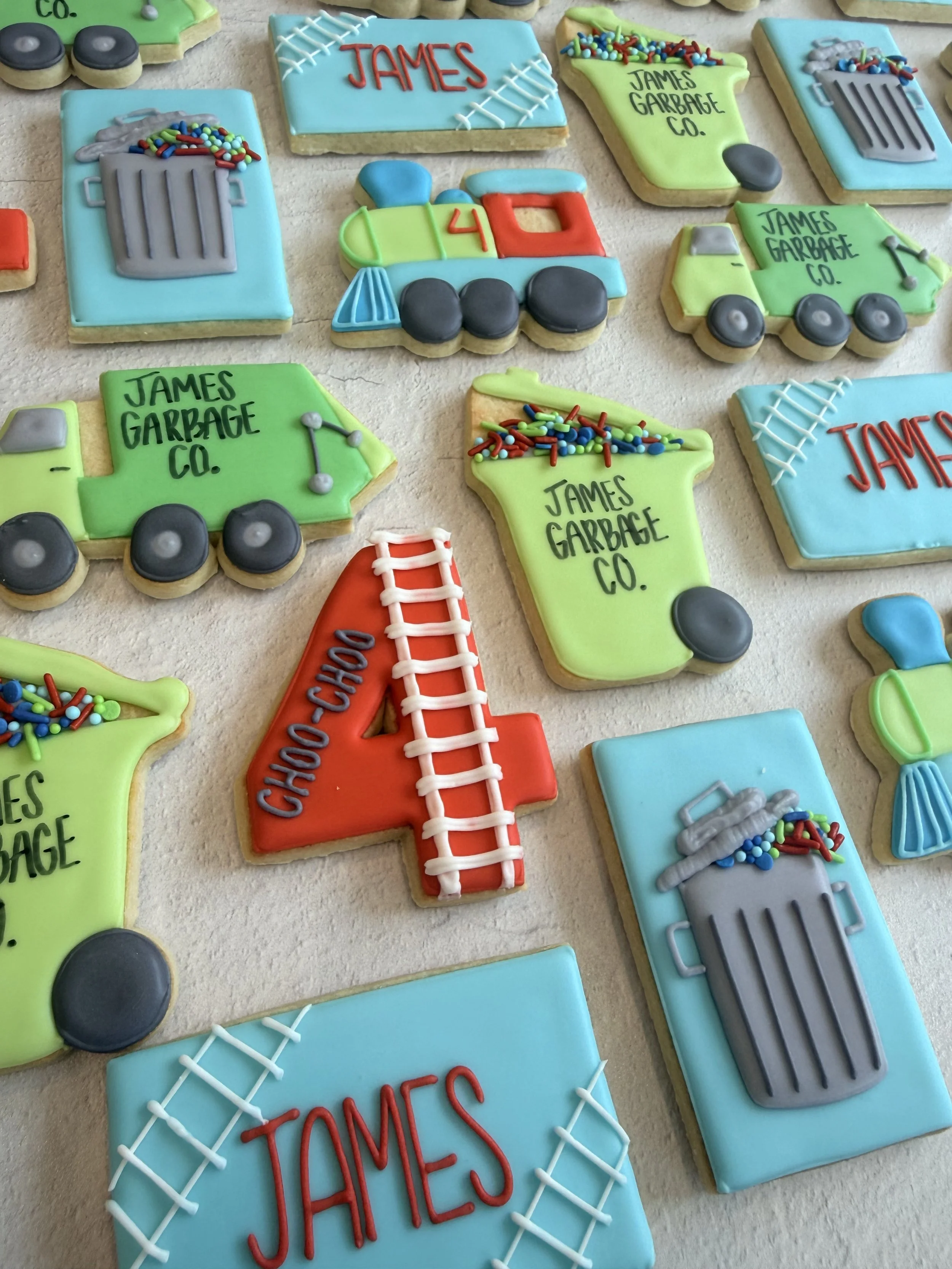 Decorated sugar cookies with themes of garbage trucks, a baseball, and text for James Garsage Co. in various colors and designs.