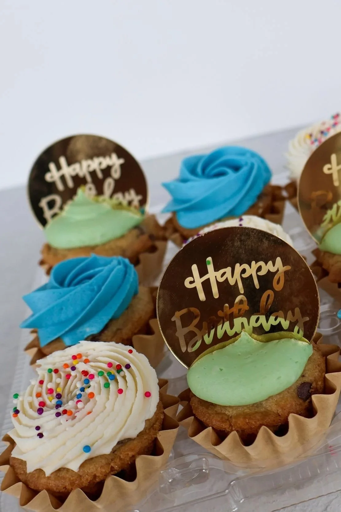 Assorted birthday cupcakes with colorful frosting and sprinkles, some with 'Happy Birthday' toppers.