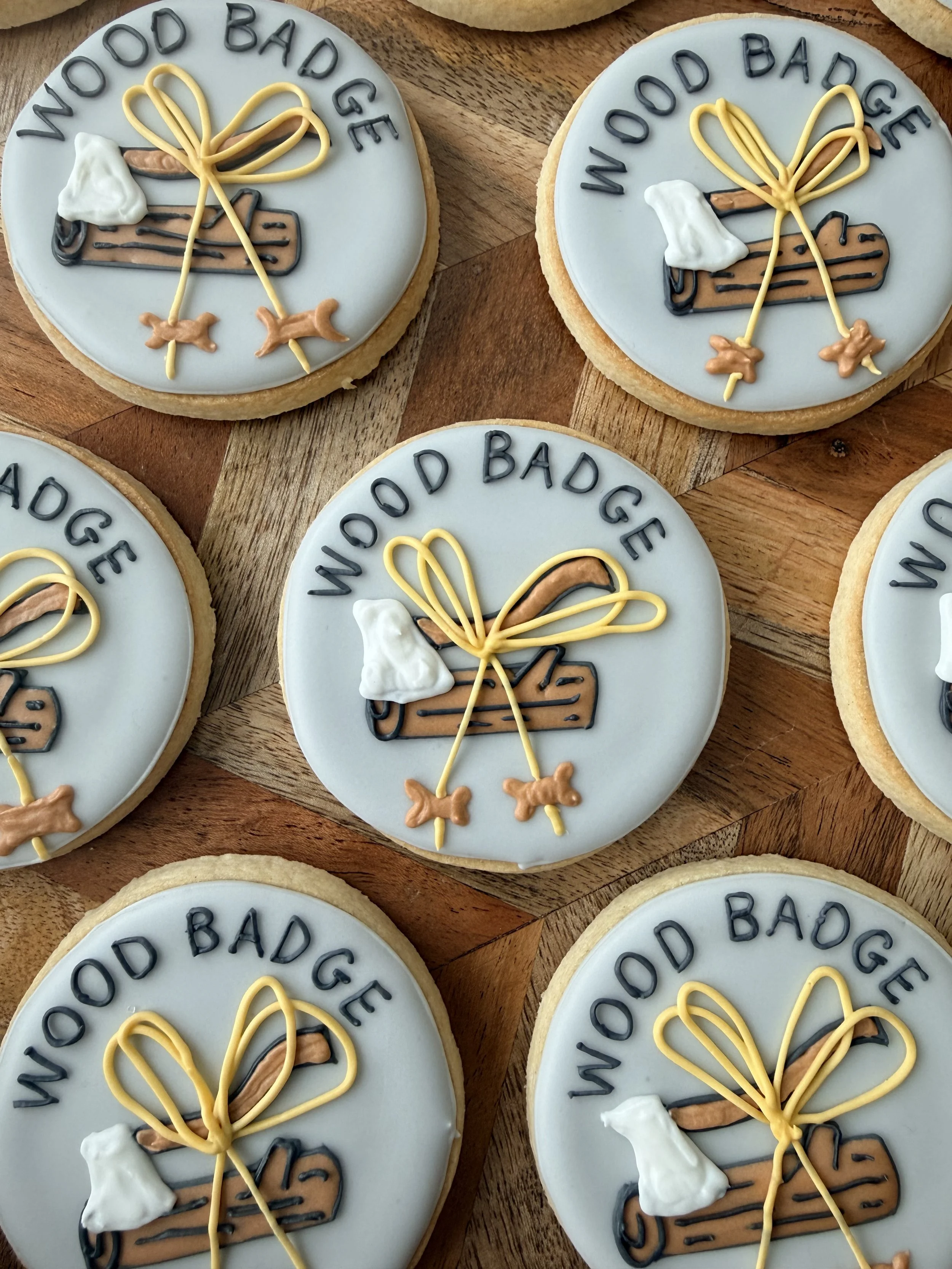 Decorative cookies with white icing, featuring the text "WOW GOOD BAD BAD" in black icing, a brown stick with black details resembling a cigar, white icing resembling smoke, and yellow icing forming a bow with strings and small orange bows, placed on