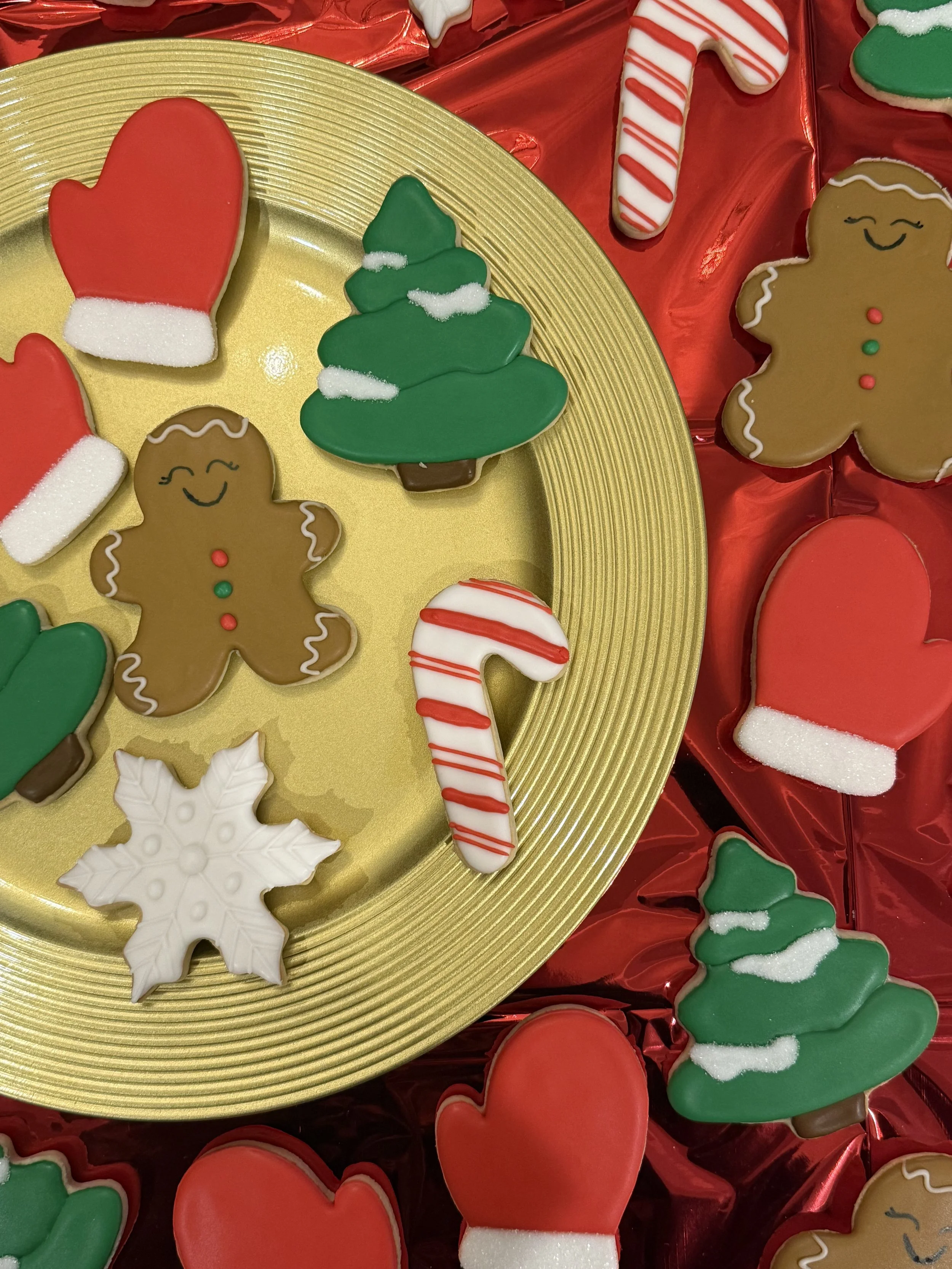 Assorted Christmas cookies on a gold tray and red background, including gingerbread men, Christmas trees, hearts, snowflakes, and candy canes decorated with icing and sugar.