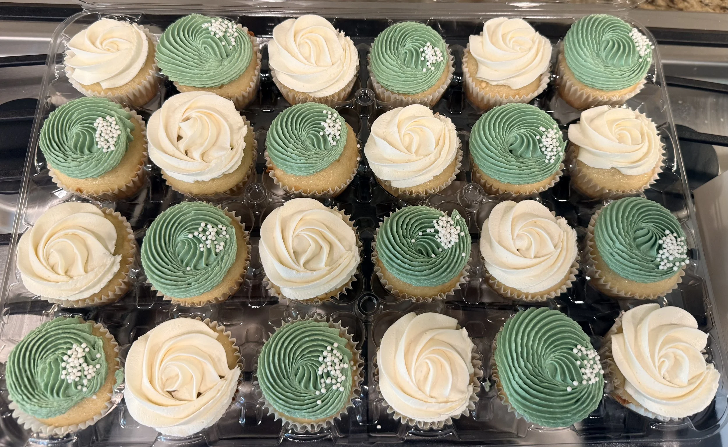 A tray of cupcakes decorated with green and white frosting, some topped with white sprinkles.