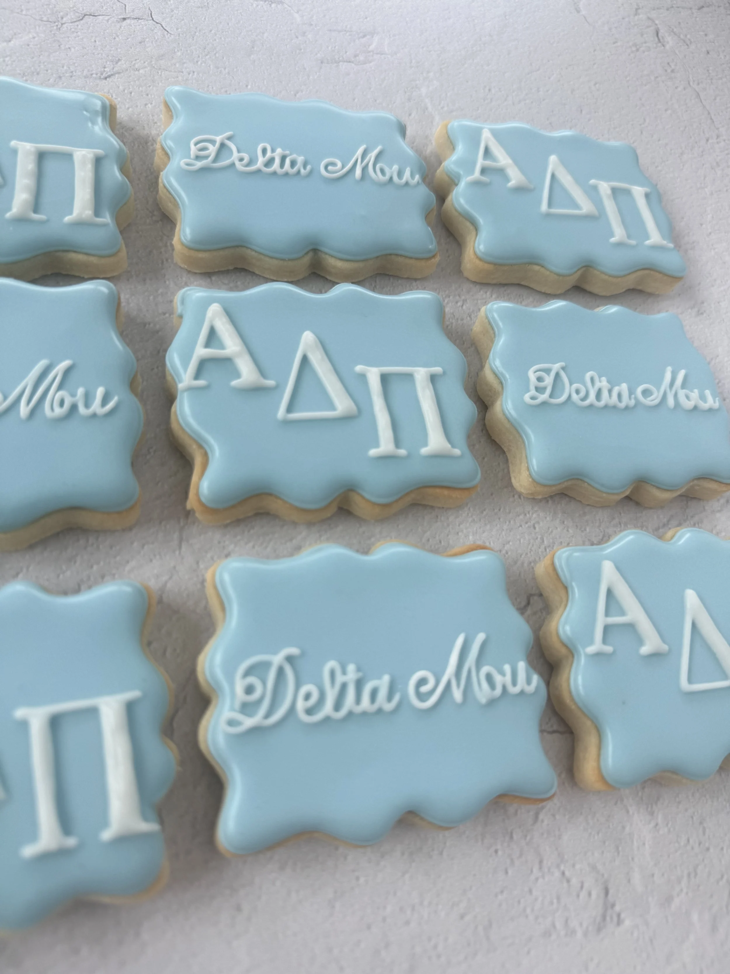 Cookies decorated with light blue icing, featuring Greek letters and the name 'Deta Mou' on some cookies.