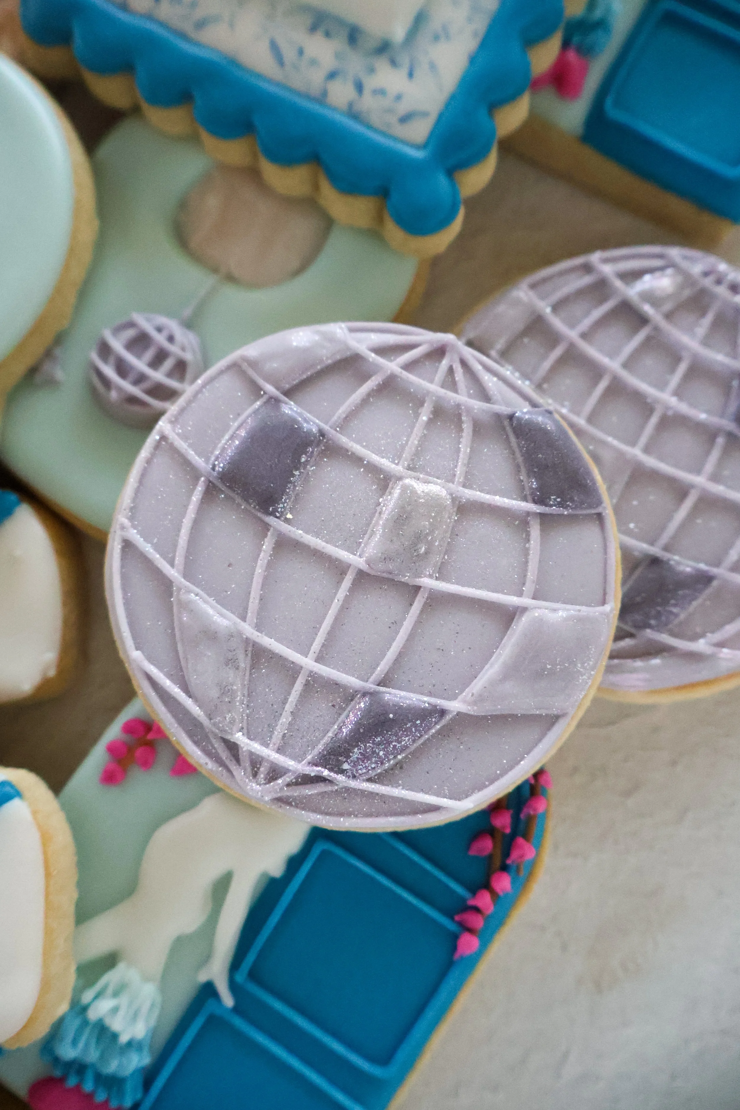Decorated cookies with blue, purple, and pink accents, some shaped like globes, on a display tray.